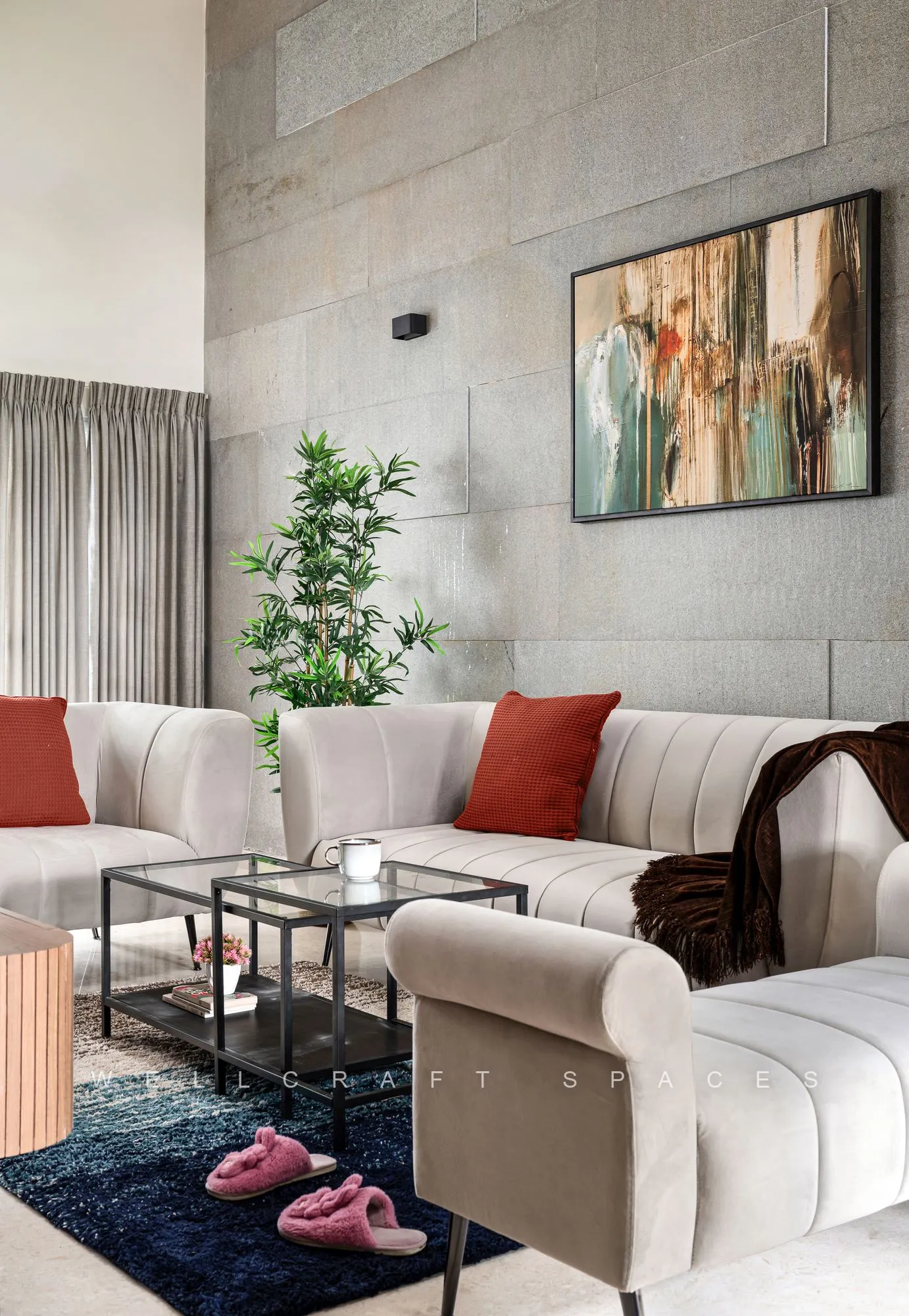 Living room with cream channel-tufted sofas, rust and blush cushions and a deep navy rug, set against a textured grey concrete wall hung with an abstract canvas.