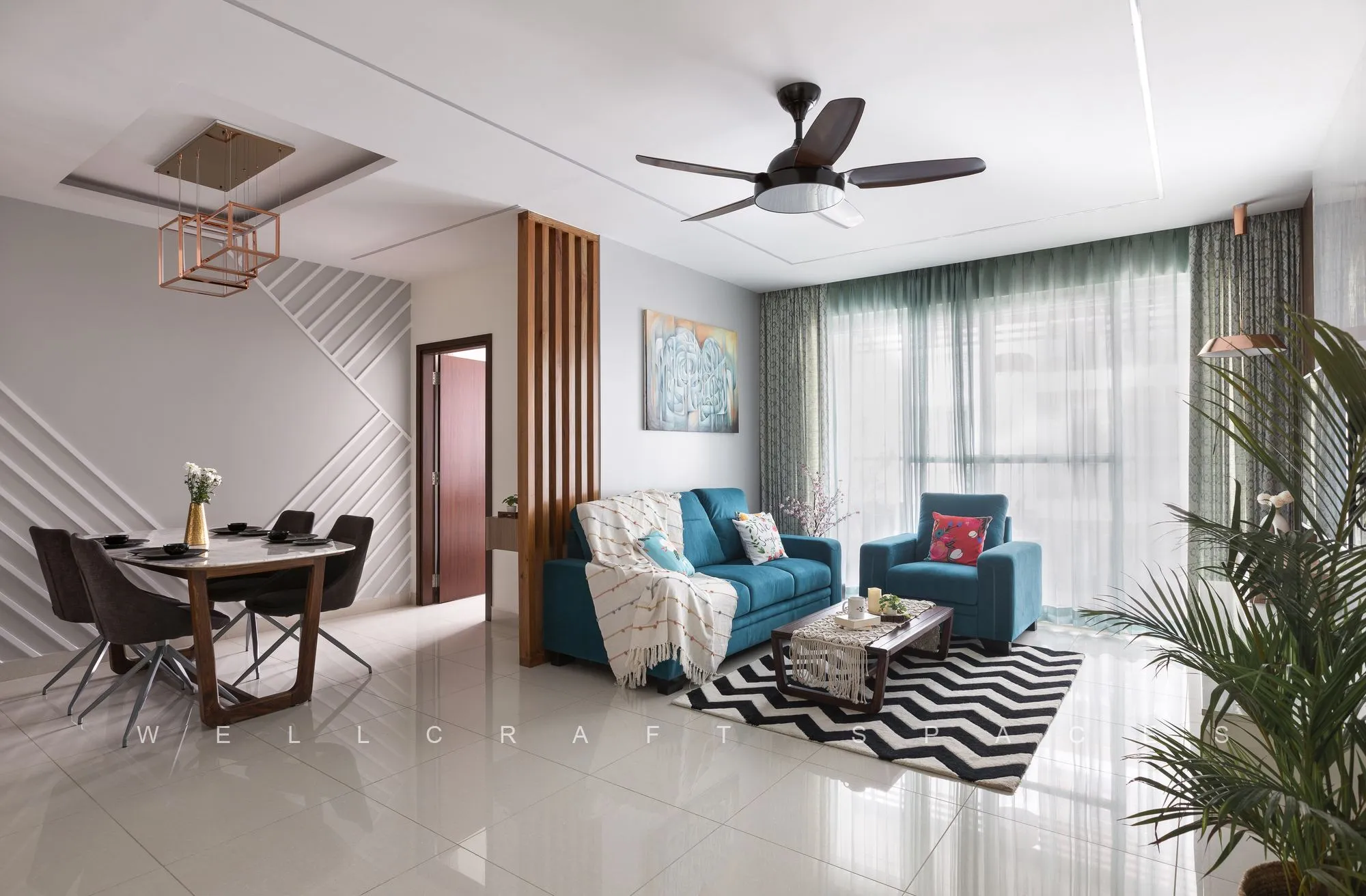 Open living and dining space with a teal fabric sofa, black-and-white chevron rug, wooden slat partition and a round dining table by the window.
