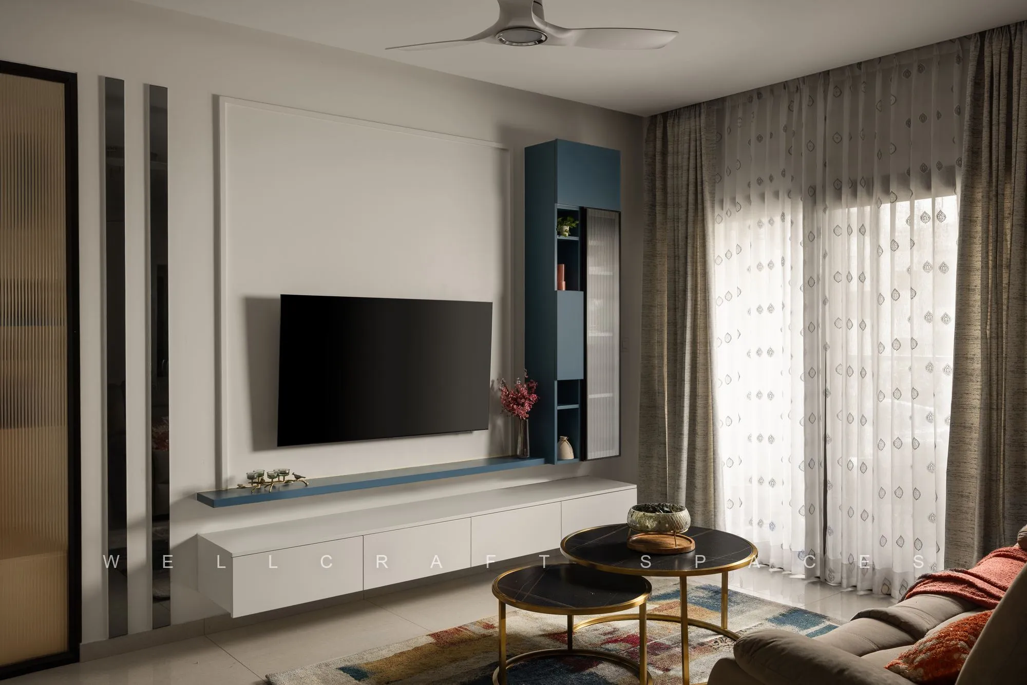 Wide living room view with a floating white media console, slate-blue tall cabinet, sheer curtains and nested black-and-brass side tables.