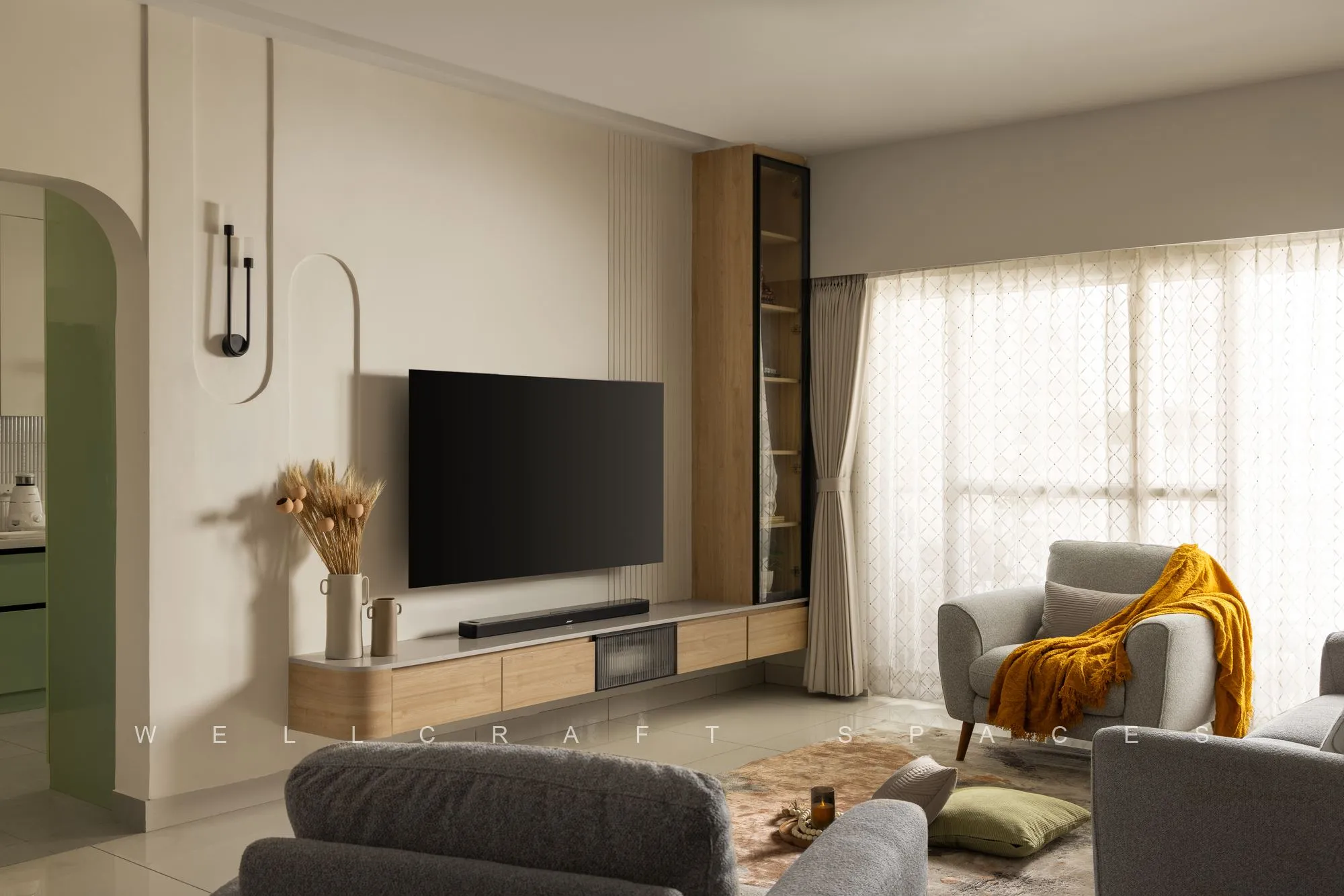 Living room in warm ivory with a wall-hung television on an oak console, grey sofas with a mustard throw and sheer curtains filling the room with light.