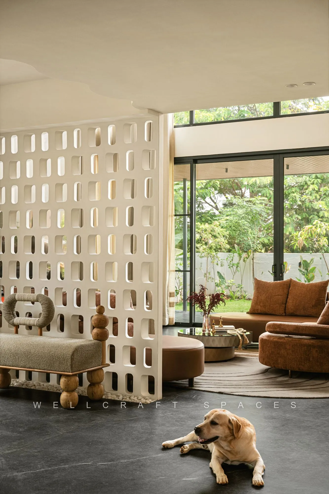 Double-height living room opening to a garden through full-height glazing, with a perforated white jaali screen and low cream sofas.