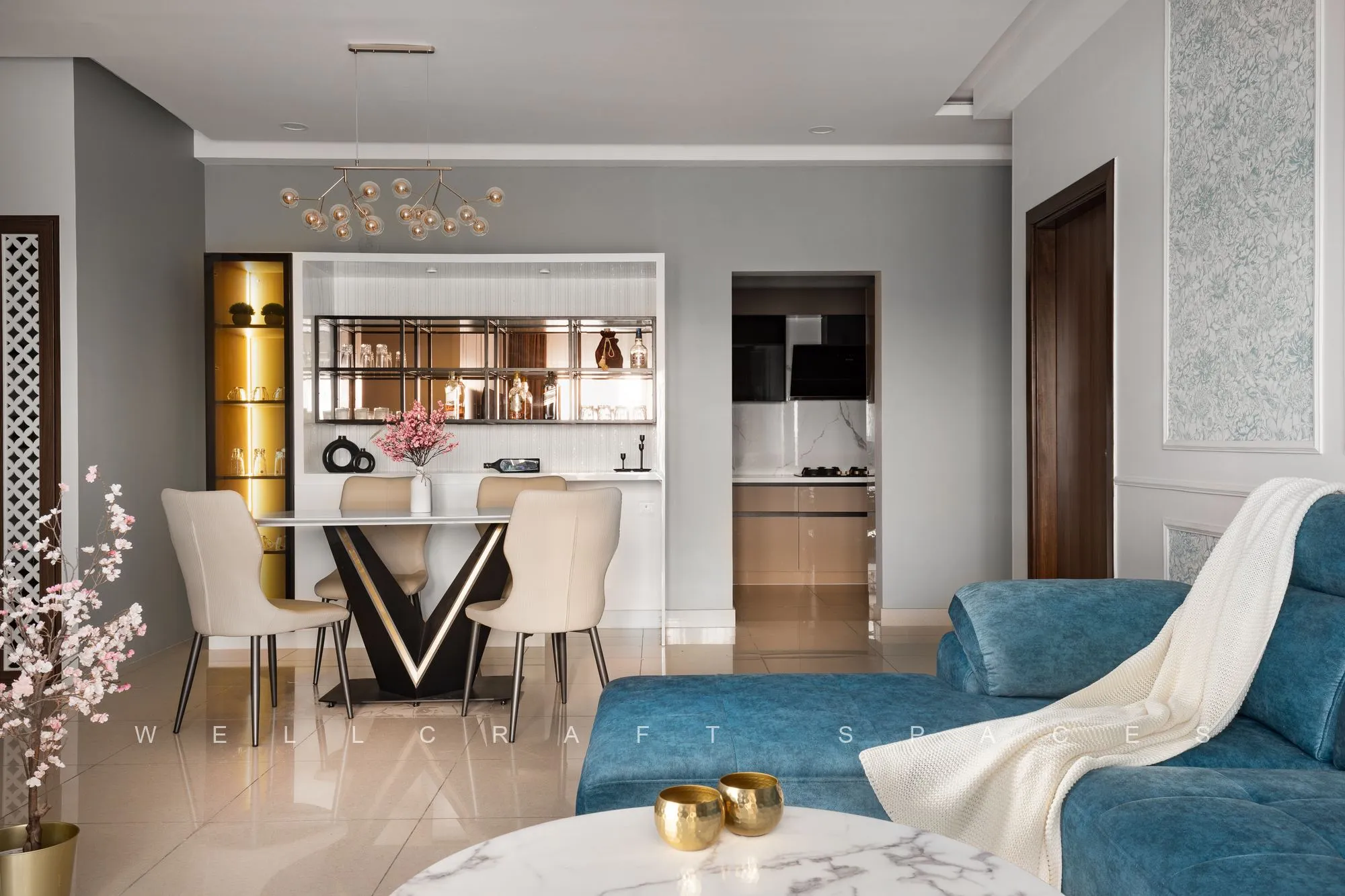 Open-plan view from the living room through to the dining area, with a teal sofa, gold-legged dining chairs and a marble-topped table under a slim fluted partition.