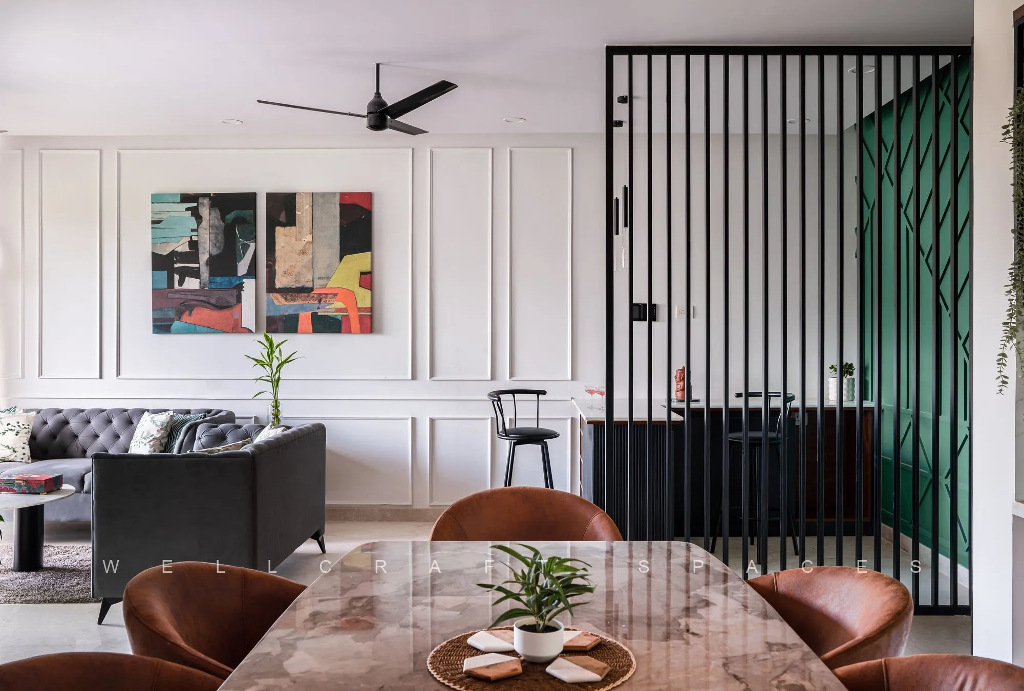 Living and dining seen together, with white moulded wall panelling, a bold abstract triptych, rust leather dining chairs around a marble table and a black slatted screen backed by green.