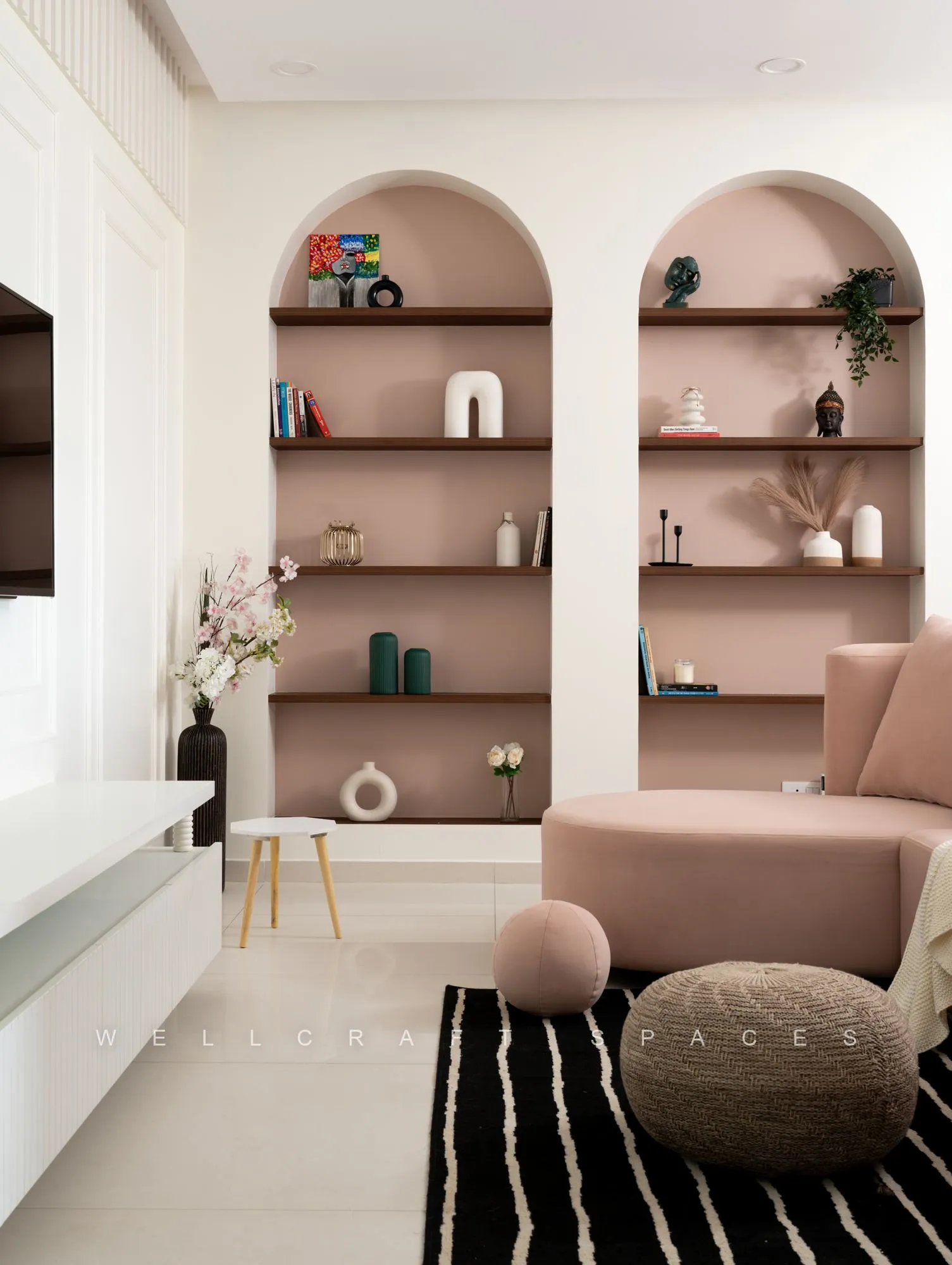Living room with a curved blush sofa, arched blush display niches with slim shelves and a black-and-white striped rug over ivory tiles.