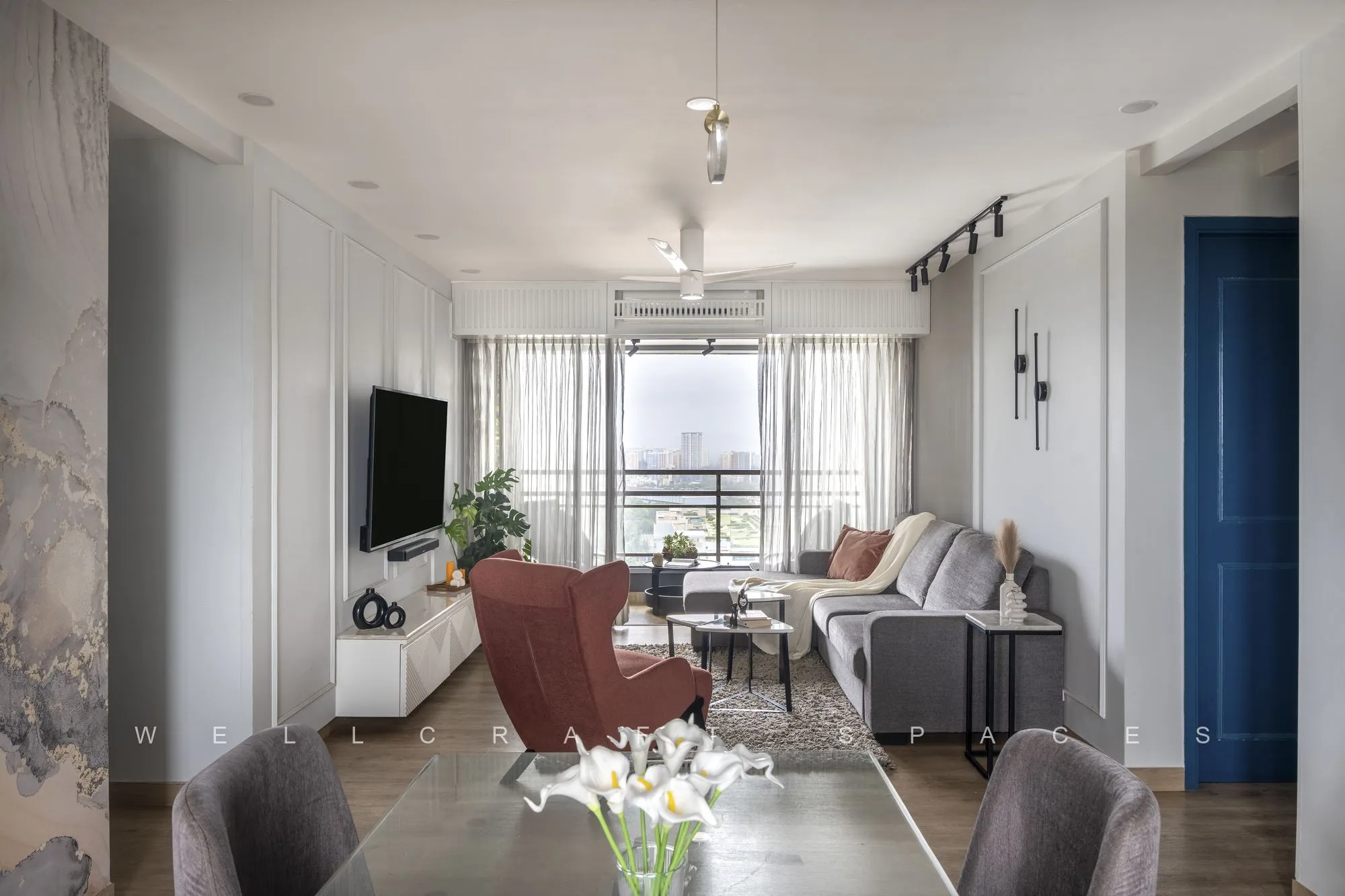 Open-plan living and dining seen end to end, with grey and rust seating, a veined marble mural wall, white wall panelling and city windows at the far end.