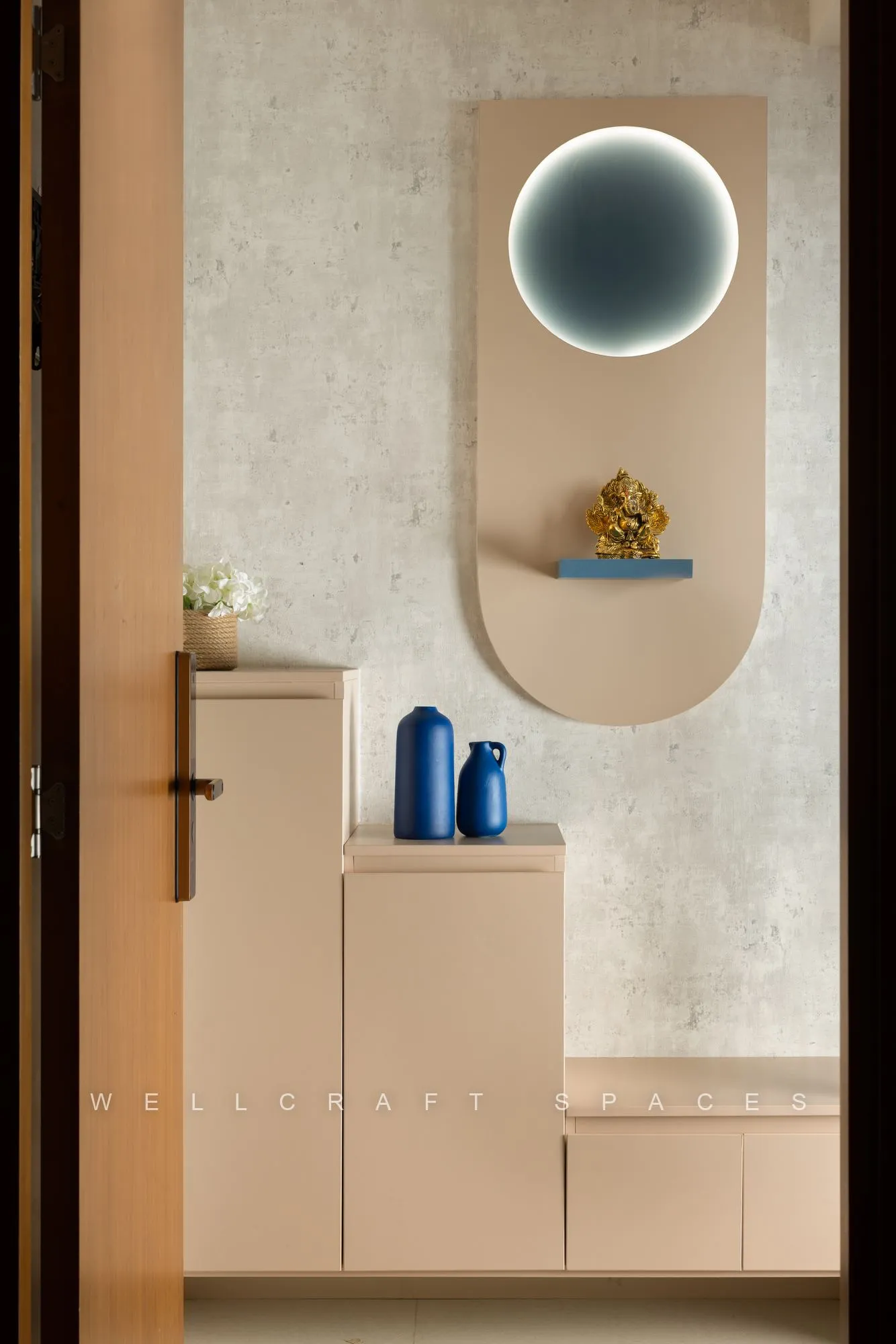 Entrance foyer with a beige arched niche set into a textured plaster wall, a circular backlit mirror and a slim console with blue vases.