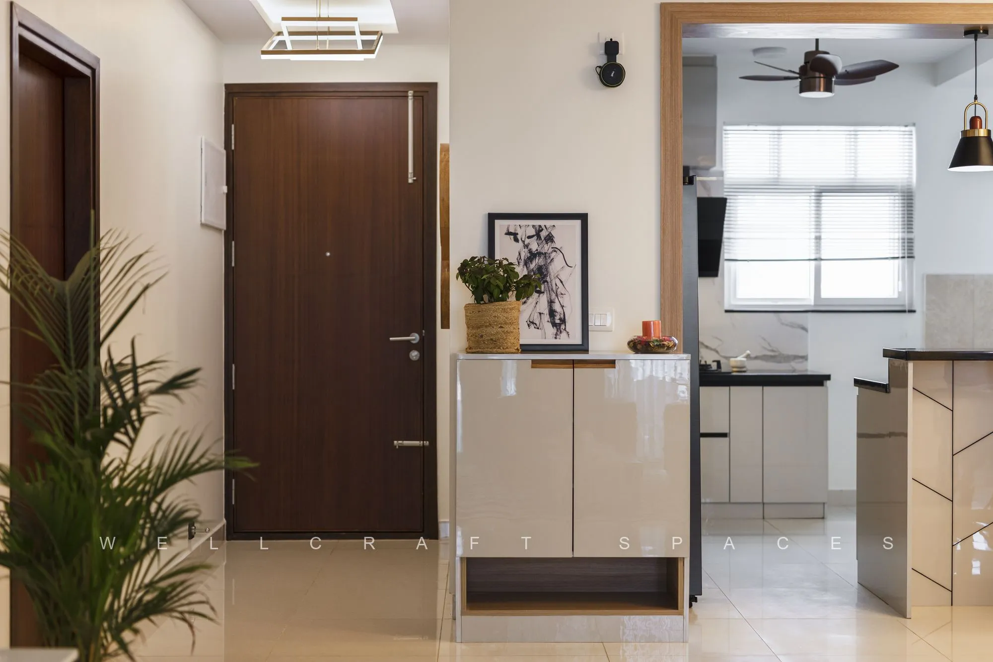 Entrance with a dark wooden door, a slim console holding a plant and framed art, looking through to the kitchen counter.