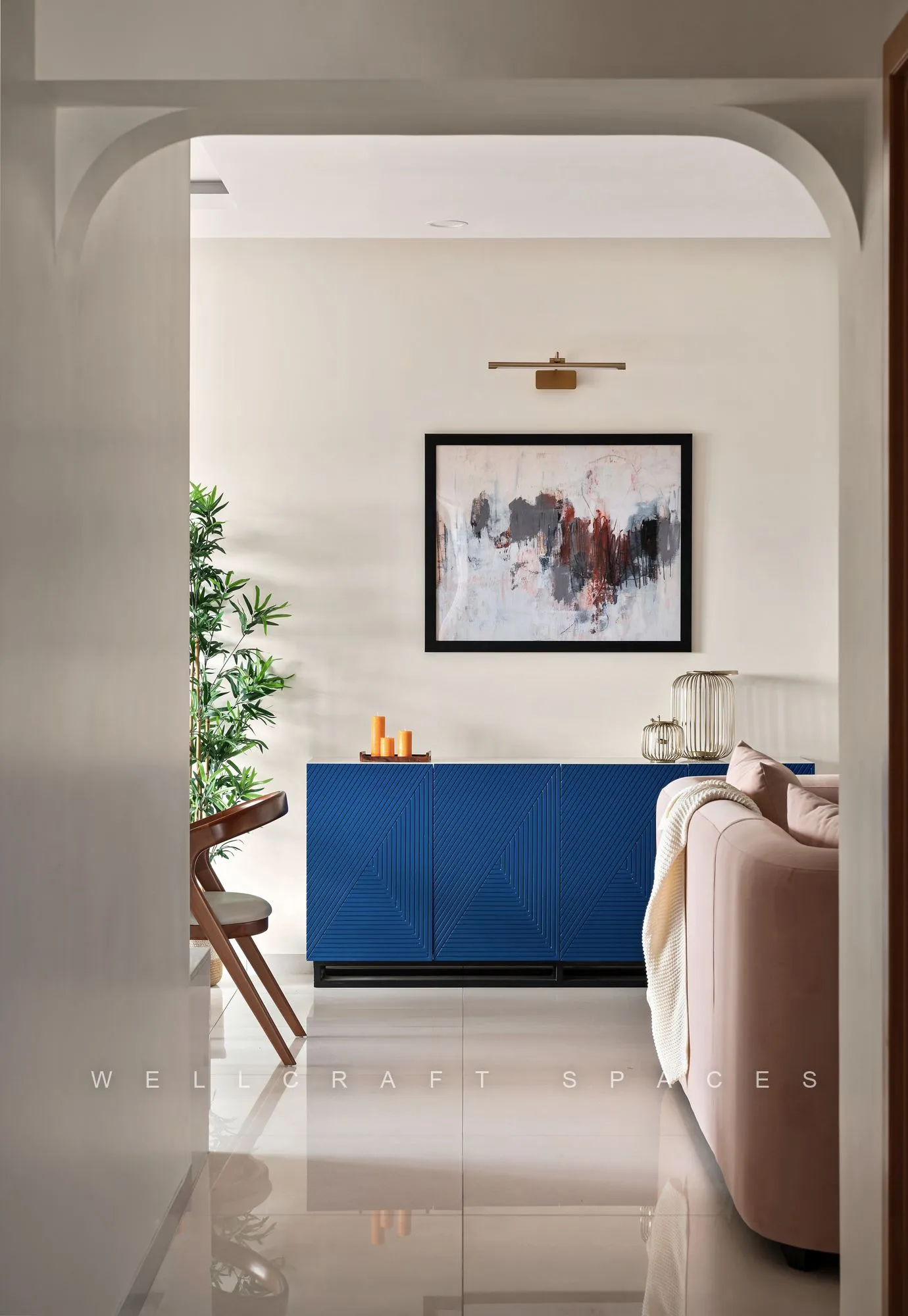 View through a softly arched opening down a glossy ivory corridor towards a cobalt-blue console and a framed landscape print.