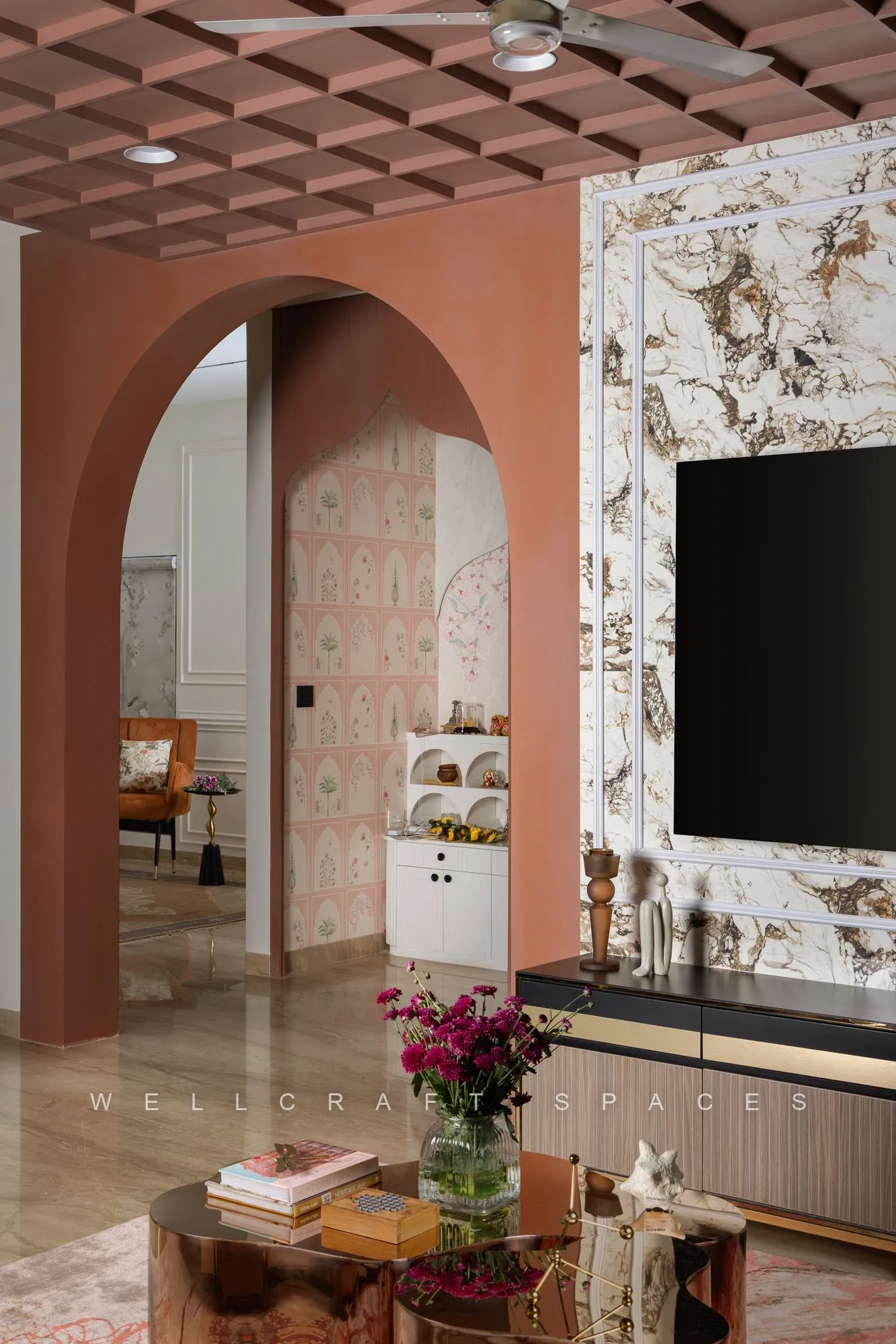 Living room looking through a terracotta plaster arch to the adjoining space, with marble cladding, a glass side table and a red patterned rug.