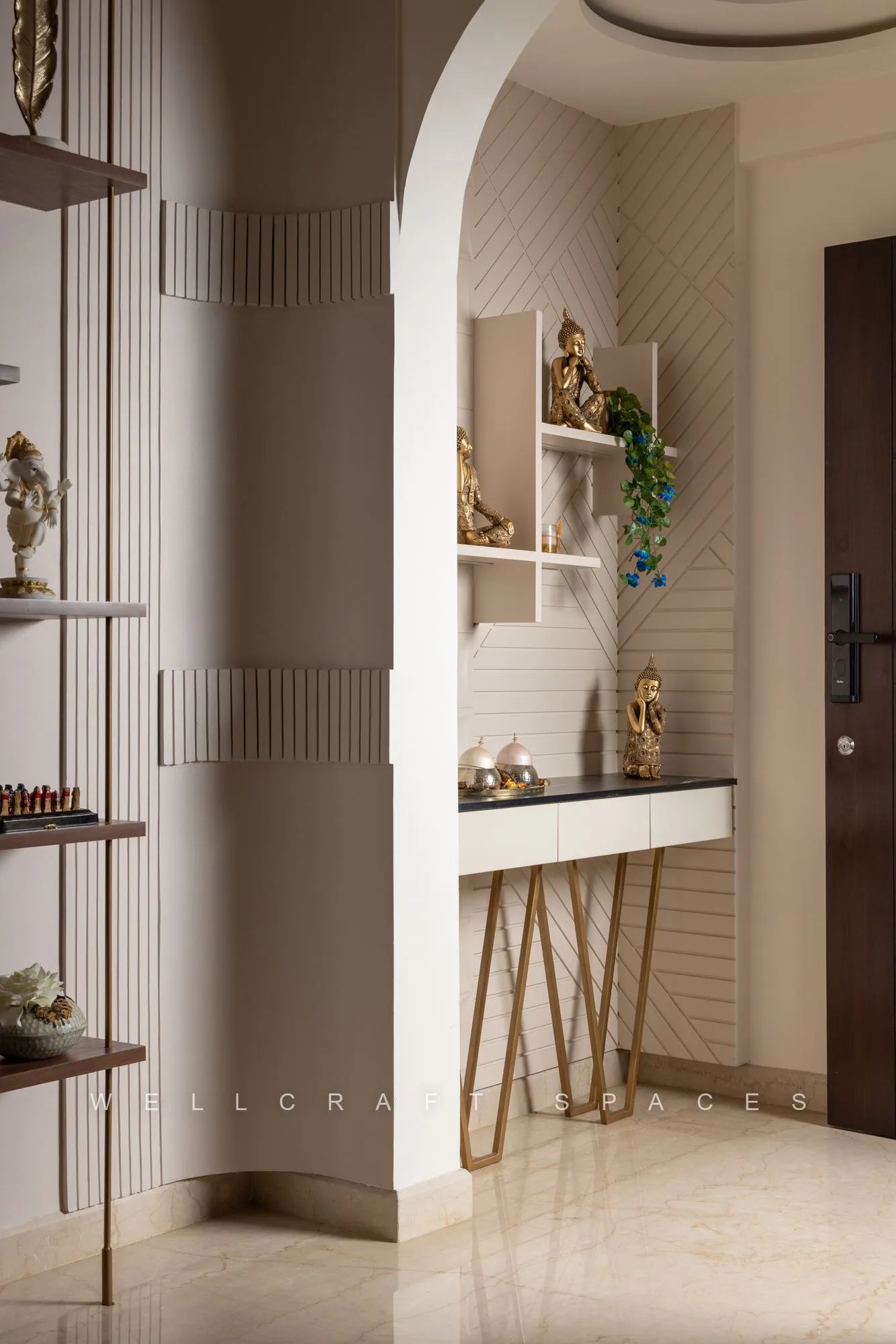 Entrance foyer with a curved fluted plaster column, a white console on brass legs, open shelving and brass idols beside the main door.