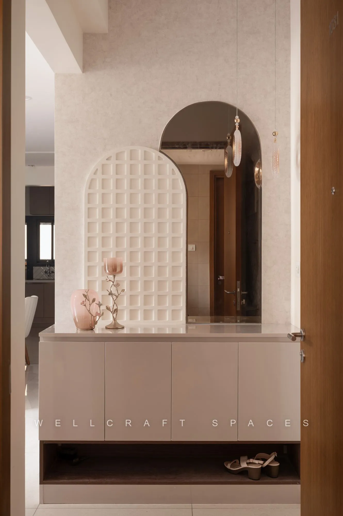Entry foyer with a blush arched niche over a low console, a woven-textured panel and an arched mirror reflecting the corridor.