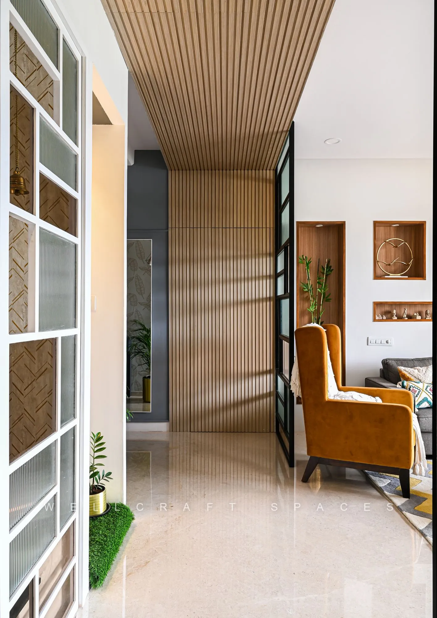Entry passage under a slatted timber ceiling, with a white glazed grid partition, a tan wing chair beyond and glossy ivory floor tiles.