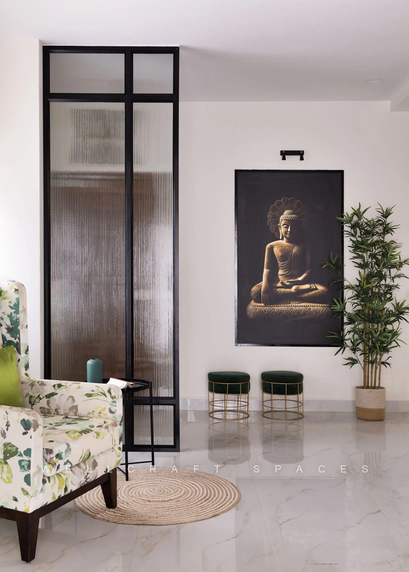 Entrance area in polished white marble with a black-framed glass partition, a large Buddha canvas, teal metal stools and a botanical-print wingback chair.