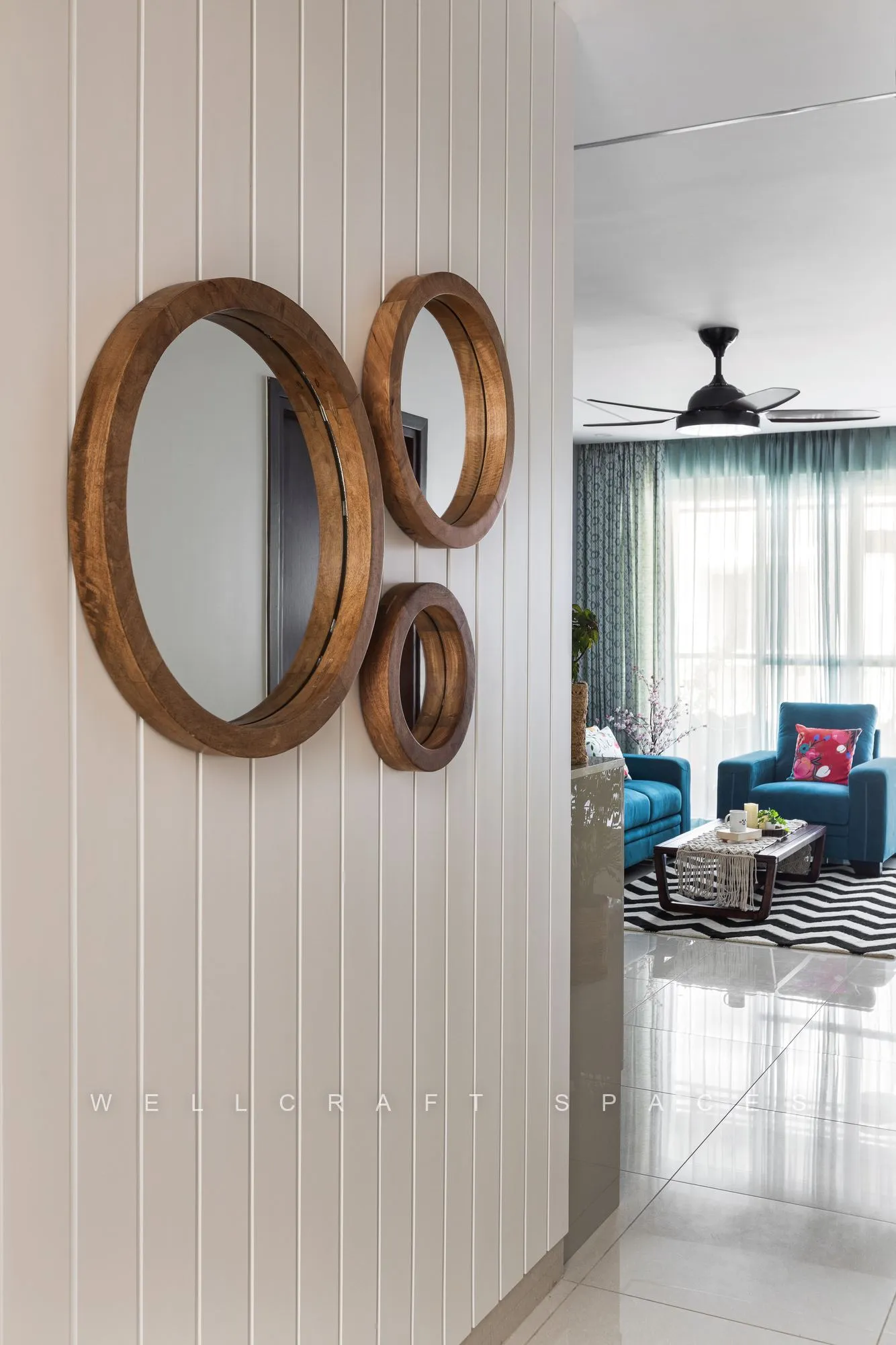Cluster of round teak-framed mirrors on a fluted white wall in the passage, reflecting the teal living room beyond.