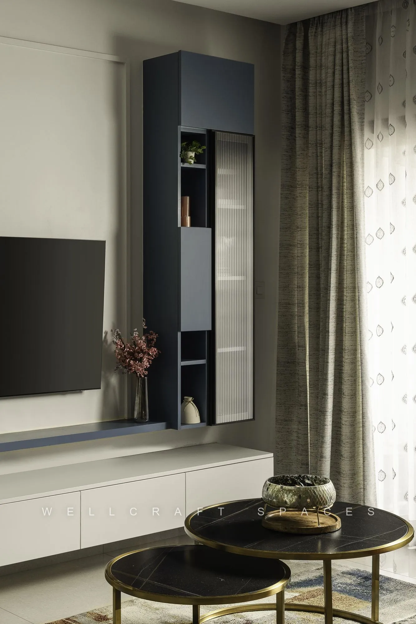 Television wall in soft white with a navy display cabinet, drapes to the floor and a pair of round black marble side tables with brass trim.