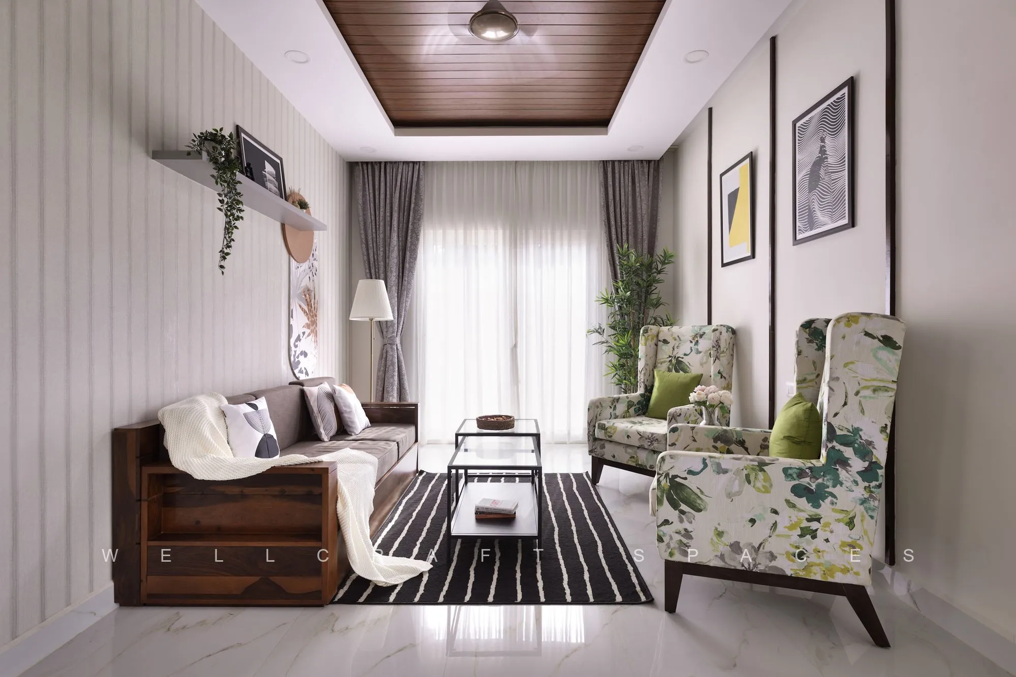 Full view of the living room showing the teak sofa, a pair of botanical-print wing chairs, a glass coffee table and a dark timber-slatted ceiling panel.