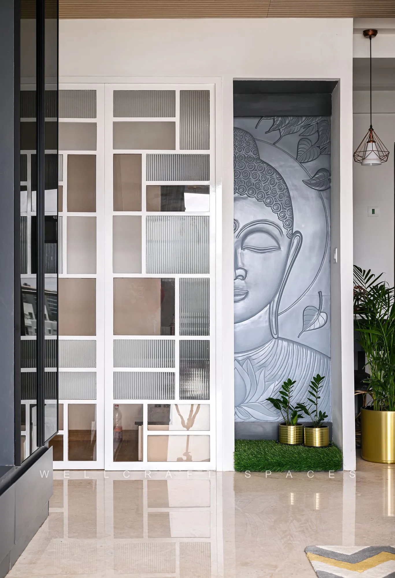 White grid partition screening a carved Buddha relief panel, with brass planters and a pendant light in the passage behind.