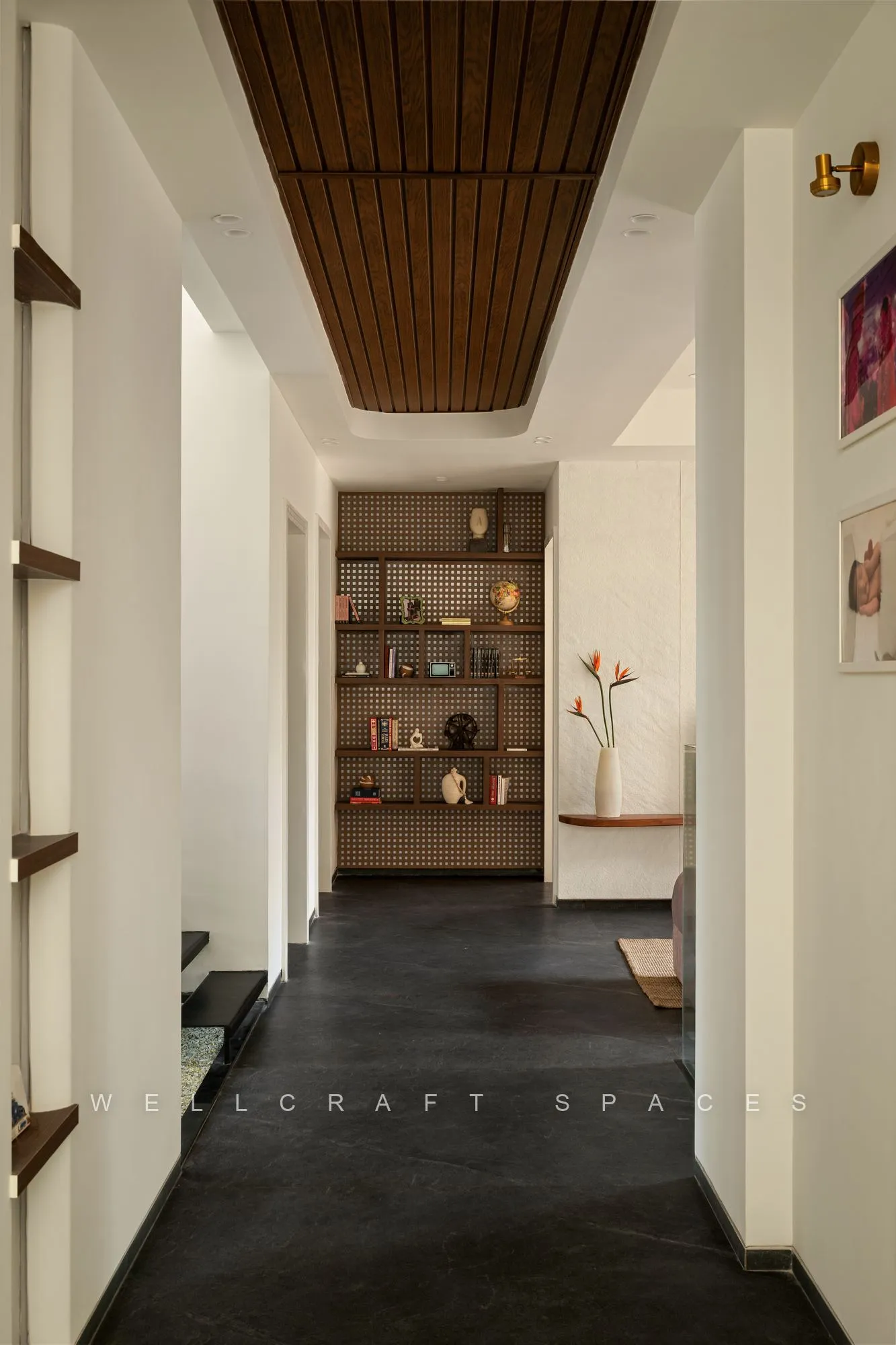 Long entry corridor with a slatted timber ceiling, charcoal stone floor and a recessed display niche lit against pale plaster walls.