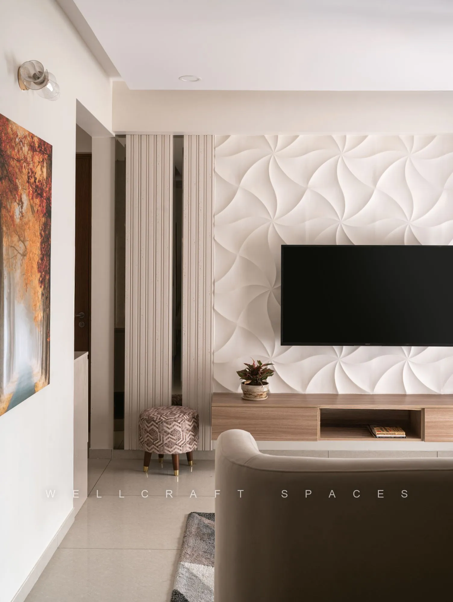 Living room framed by a faceted white 3D tile wall around the wall-mounted television, with a curved cream sofa and a warm abstract artwork.