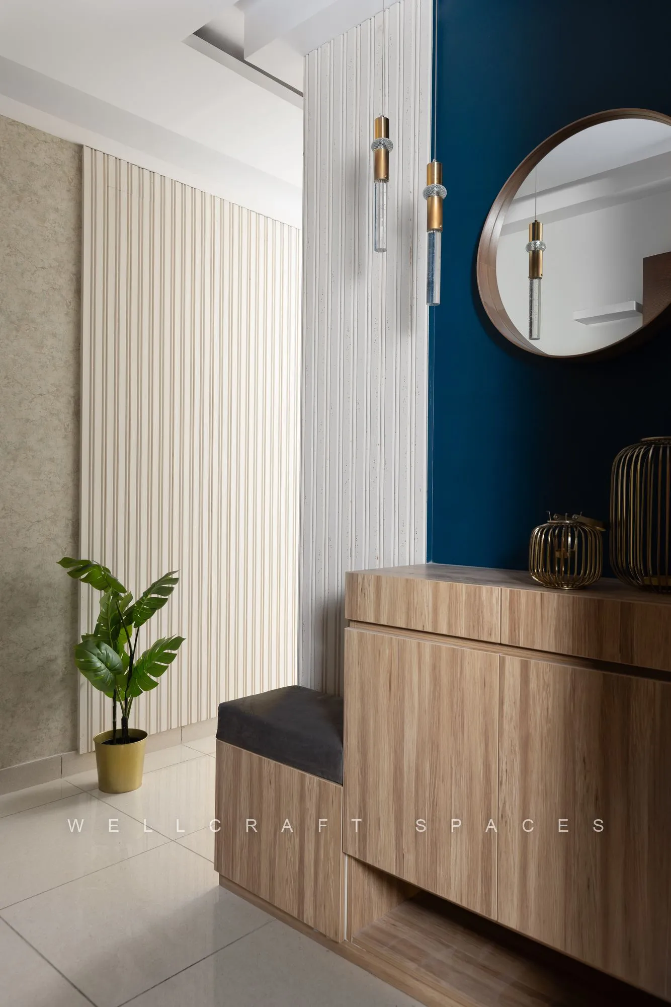 Foyer bench in warm oak beside a fluted cream wall panel, with a potted plant and a round mirror on the blue accent wall.