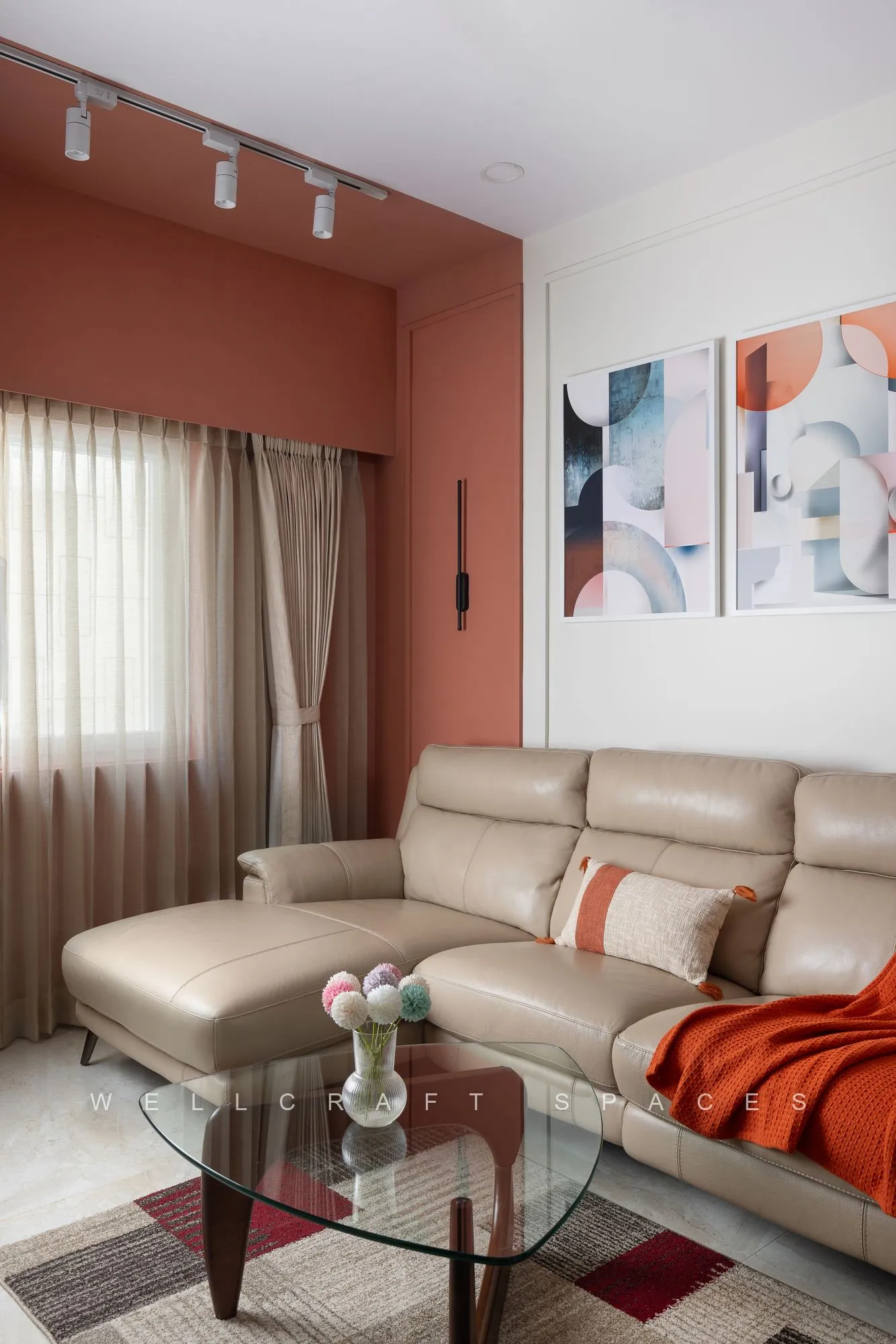 Tan leather sectional with rust cushions and a glass coffee table, against a terracotta feature wall with abstract art and track lighting above.