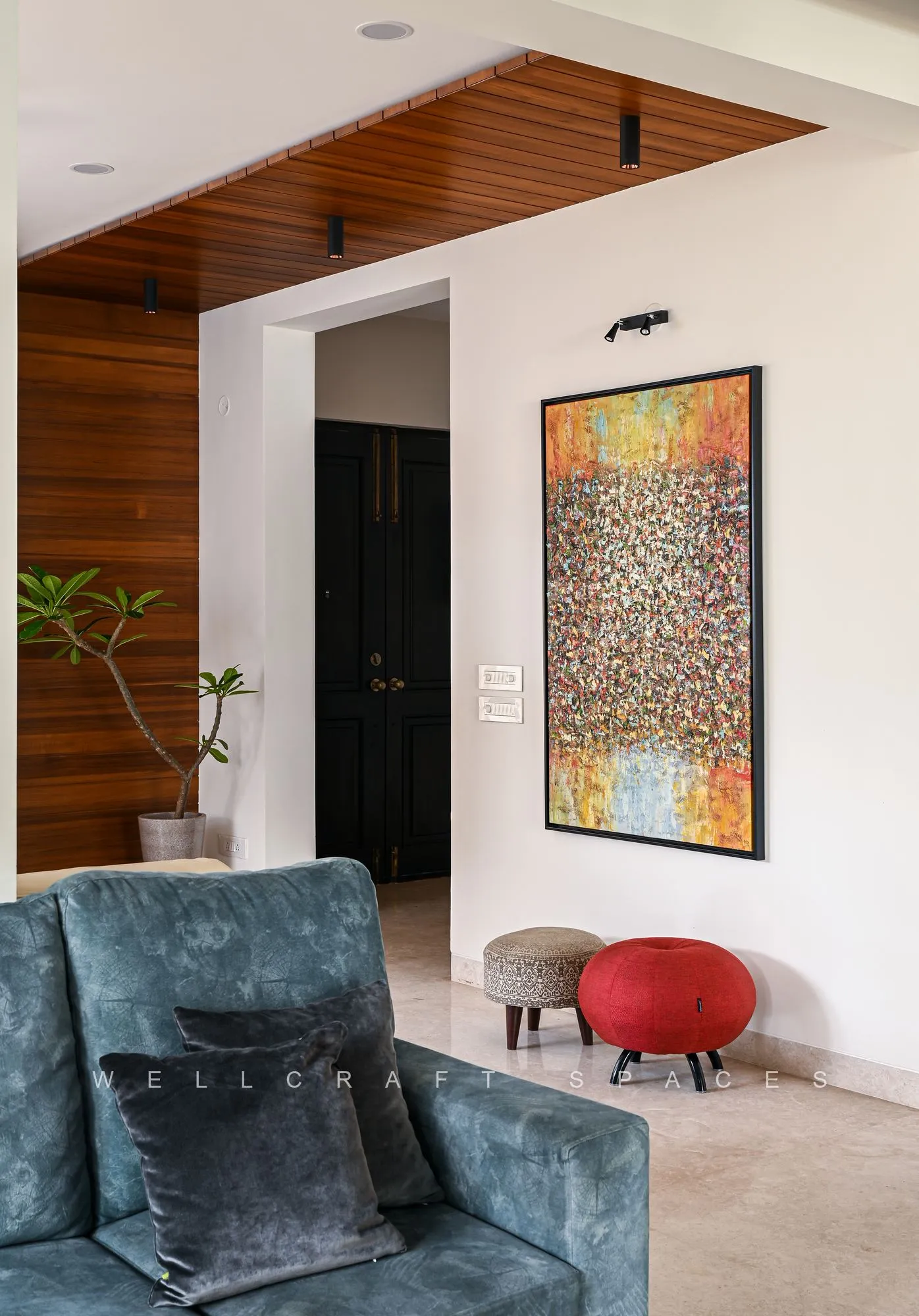 Passage from the foyer framed by a timber-lined ceiling, an arched opening and a framed artwork, with a grey upholstered chair and round red stool in the foreground.