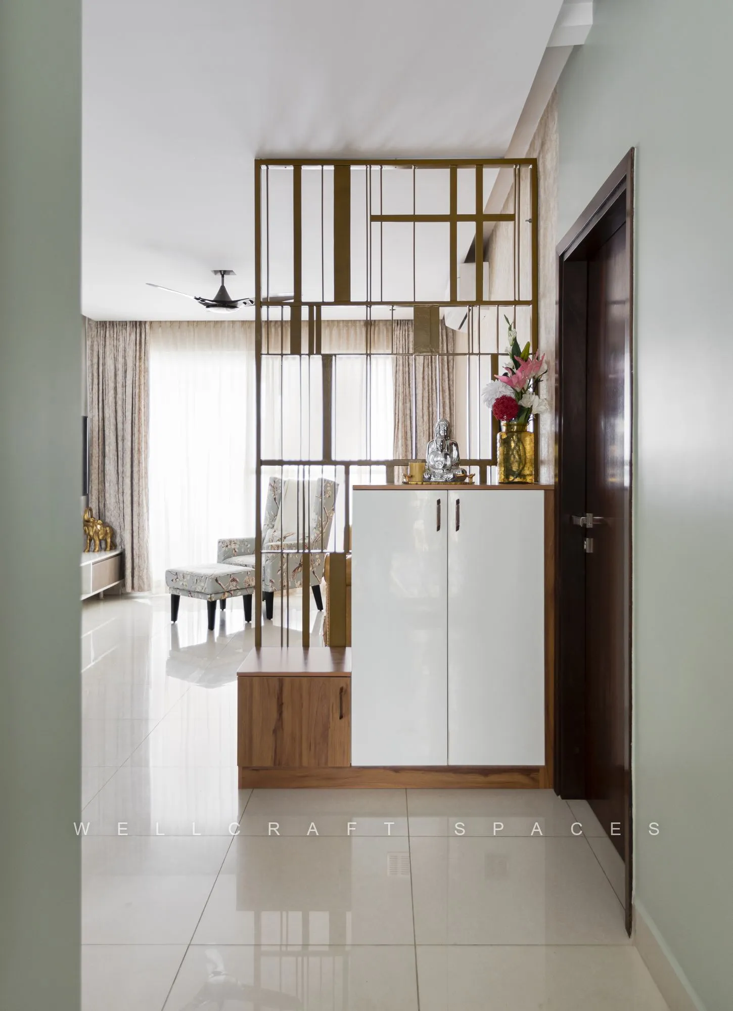 Foyer with a white shoe cabinet and a brass grid partition screening the corridor, opening onto the dining area beyond.
