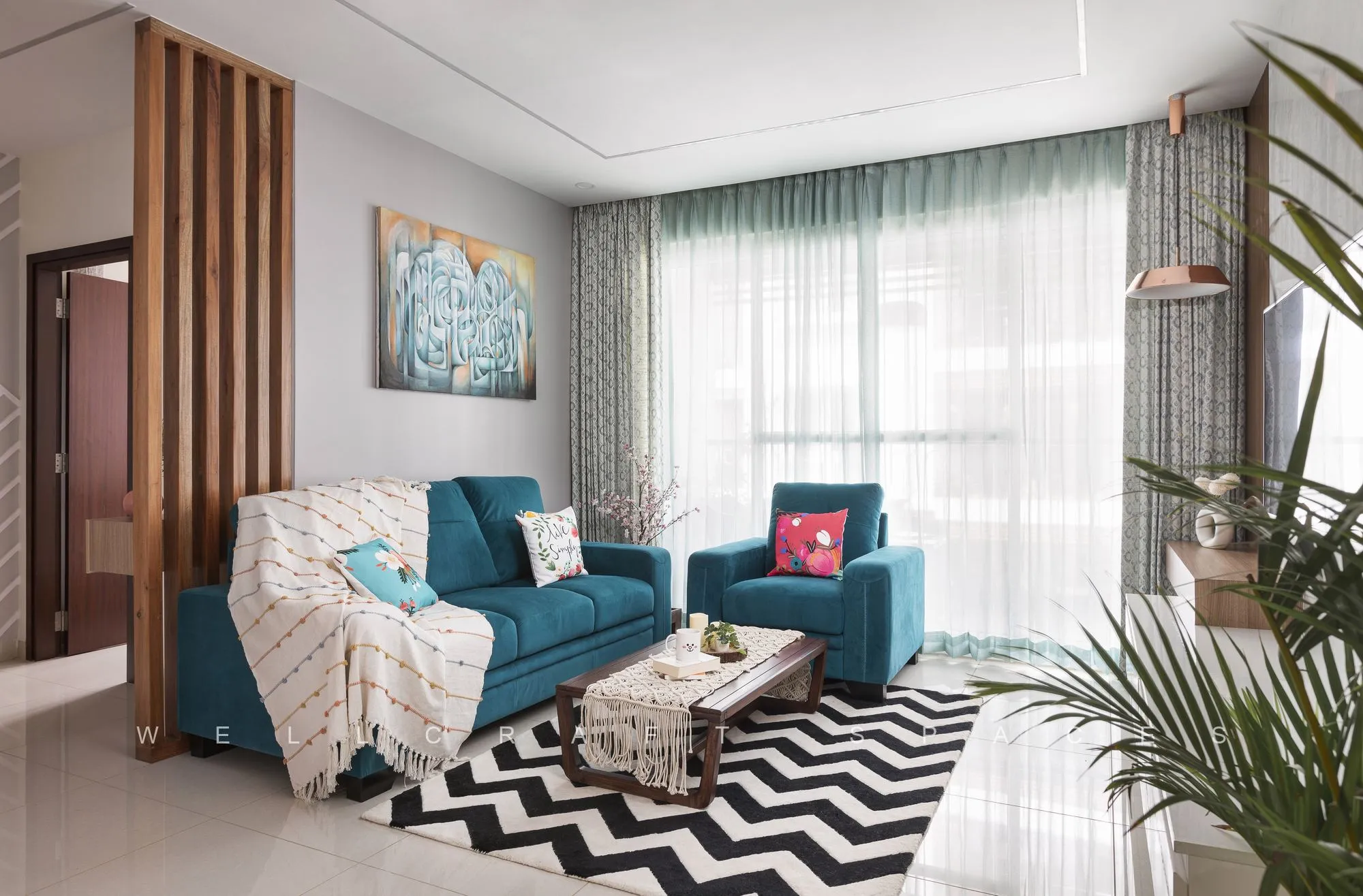 Teal sofa and armchair with red and patterned cushions on a chevron rug, framed by vertical wood battens and a green-toned artwork.