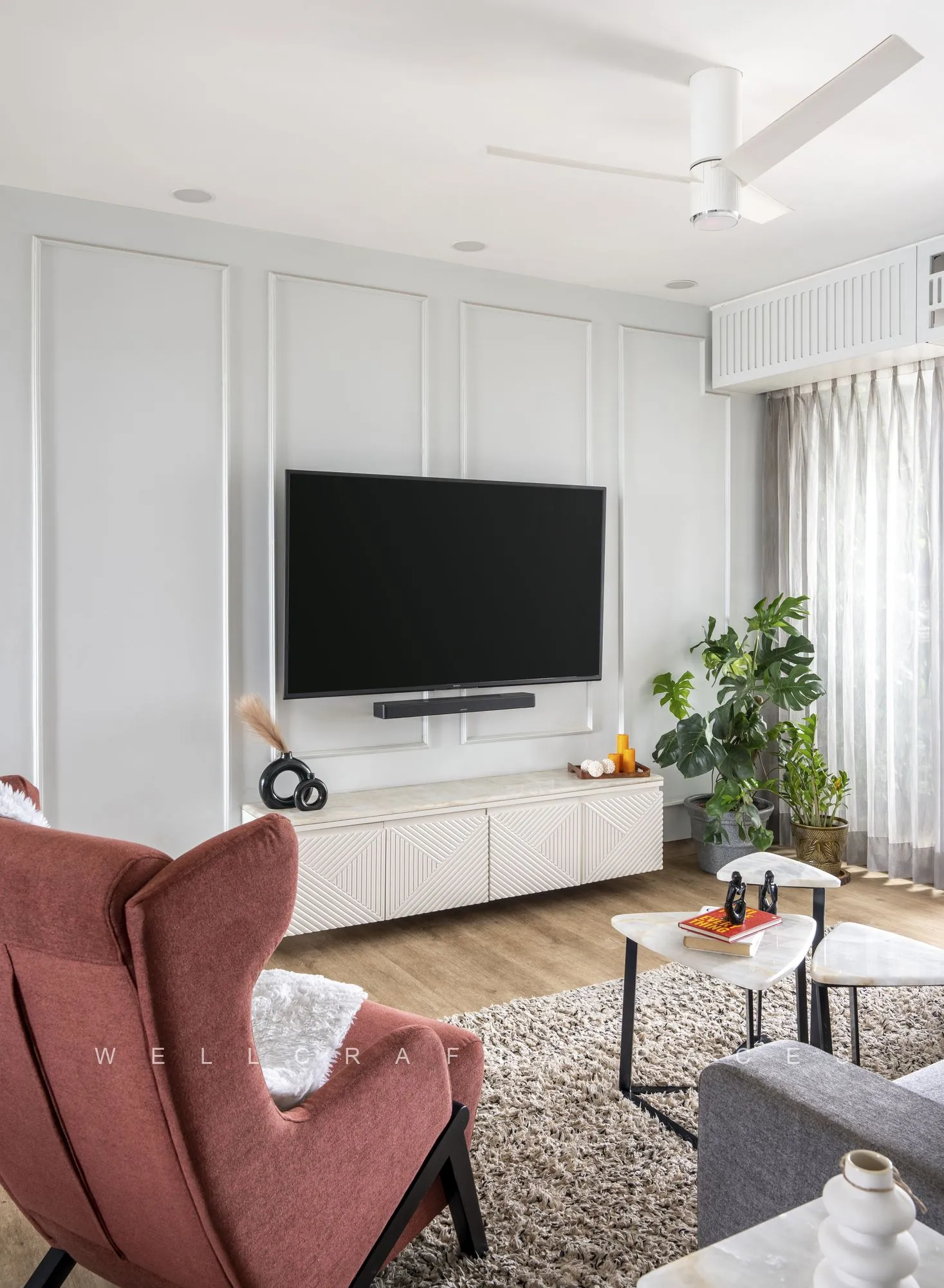 Living room media wall with a wall-mounted television over a low white console, a blush velvet wing chair and a shaggy grey rug on oak flooring.
