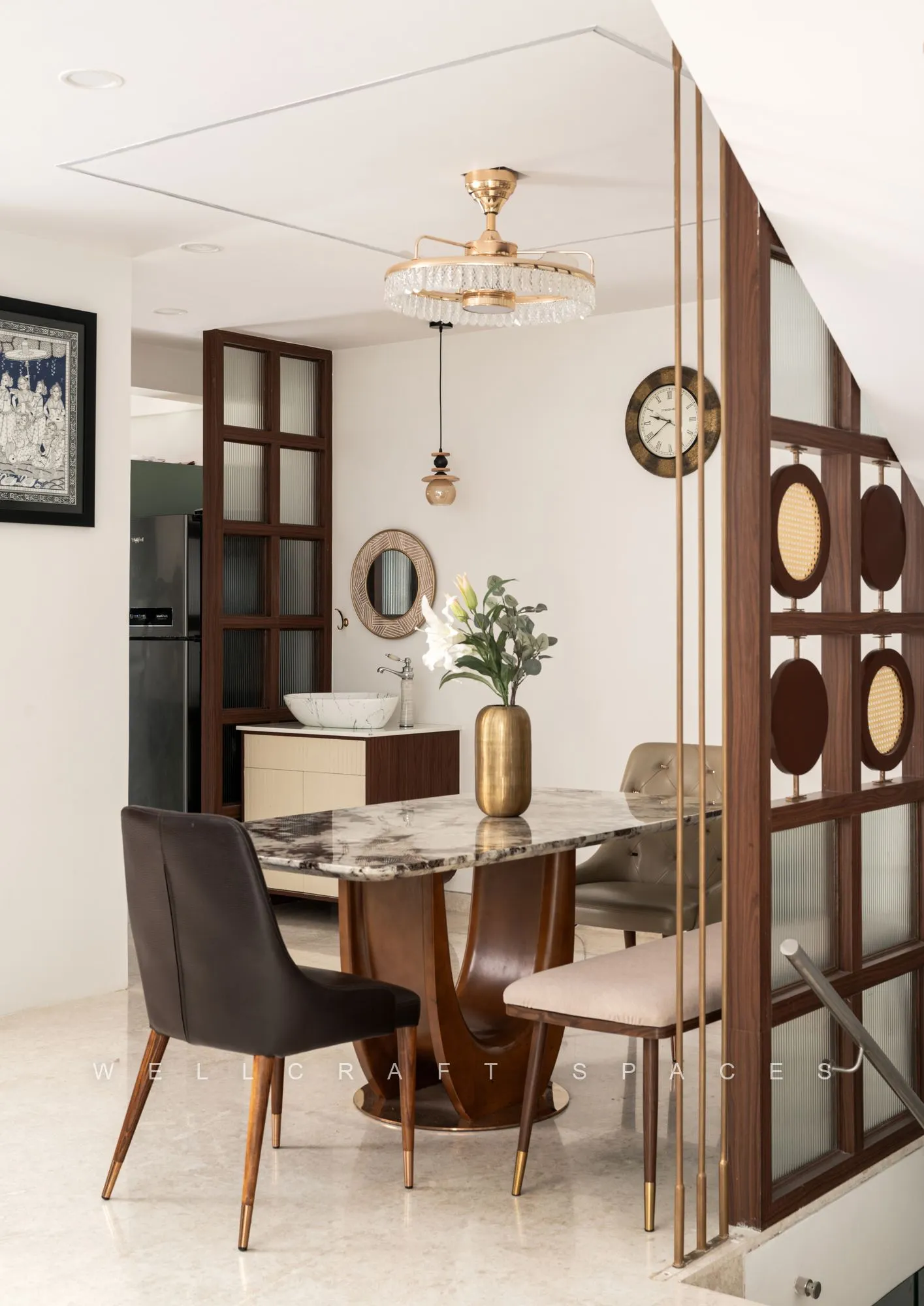 Dining area seen through a carved walnut and fluted-glass screen, with a marble-top table, tan and grey leather chairs and a crystal chandelier overhead.
