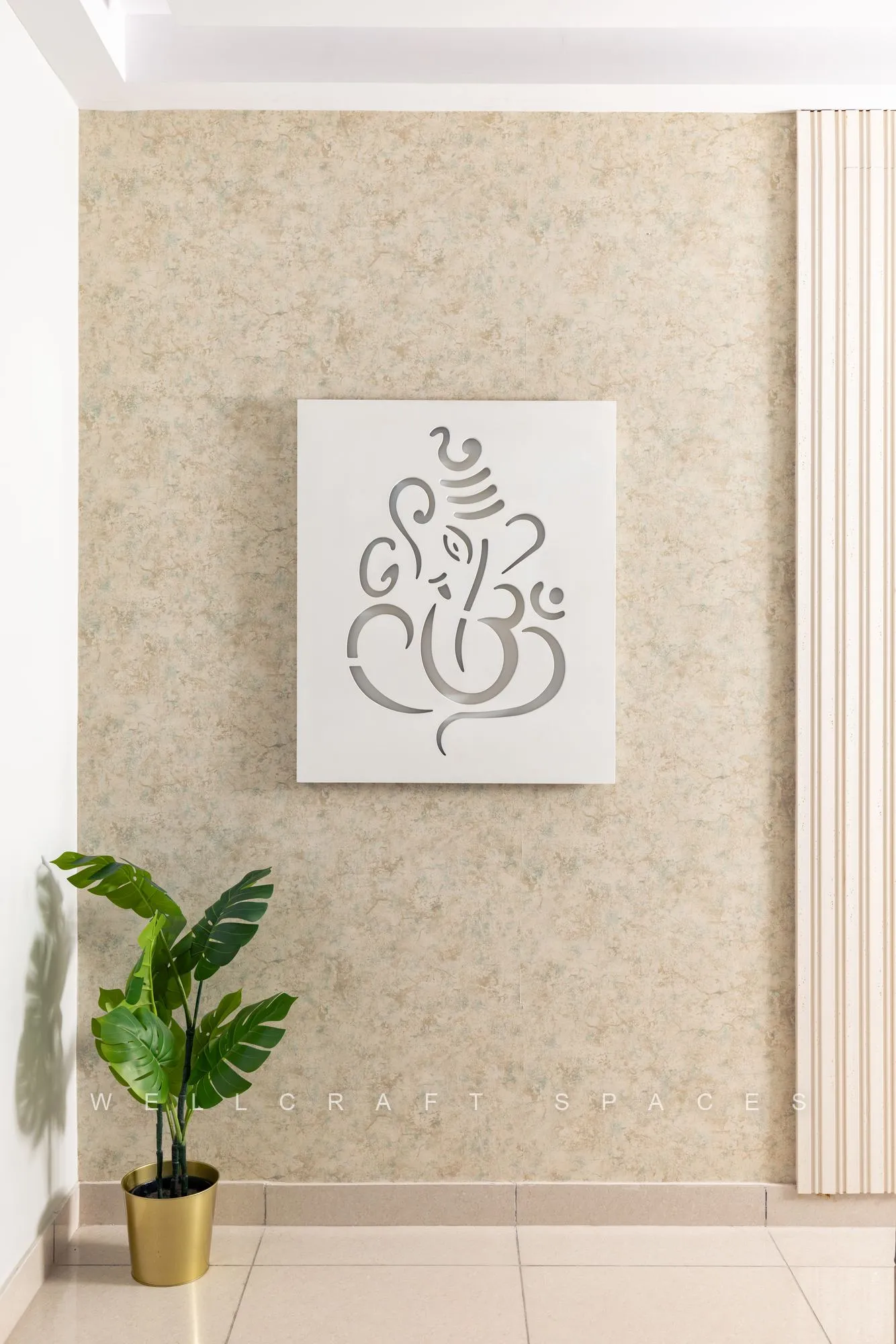Framed line-art Ganesha canvas on a soft damask-textured wall, flanked by fluted panelling and a brass planter.
