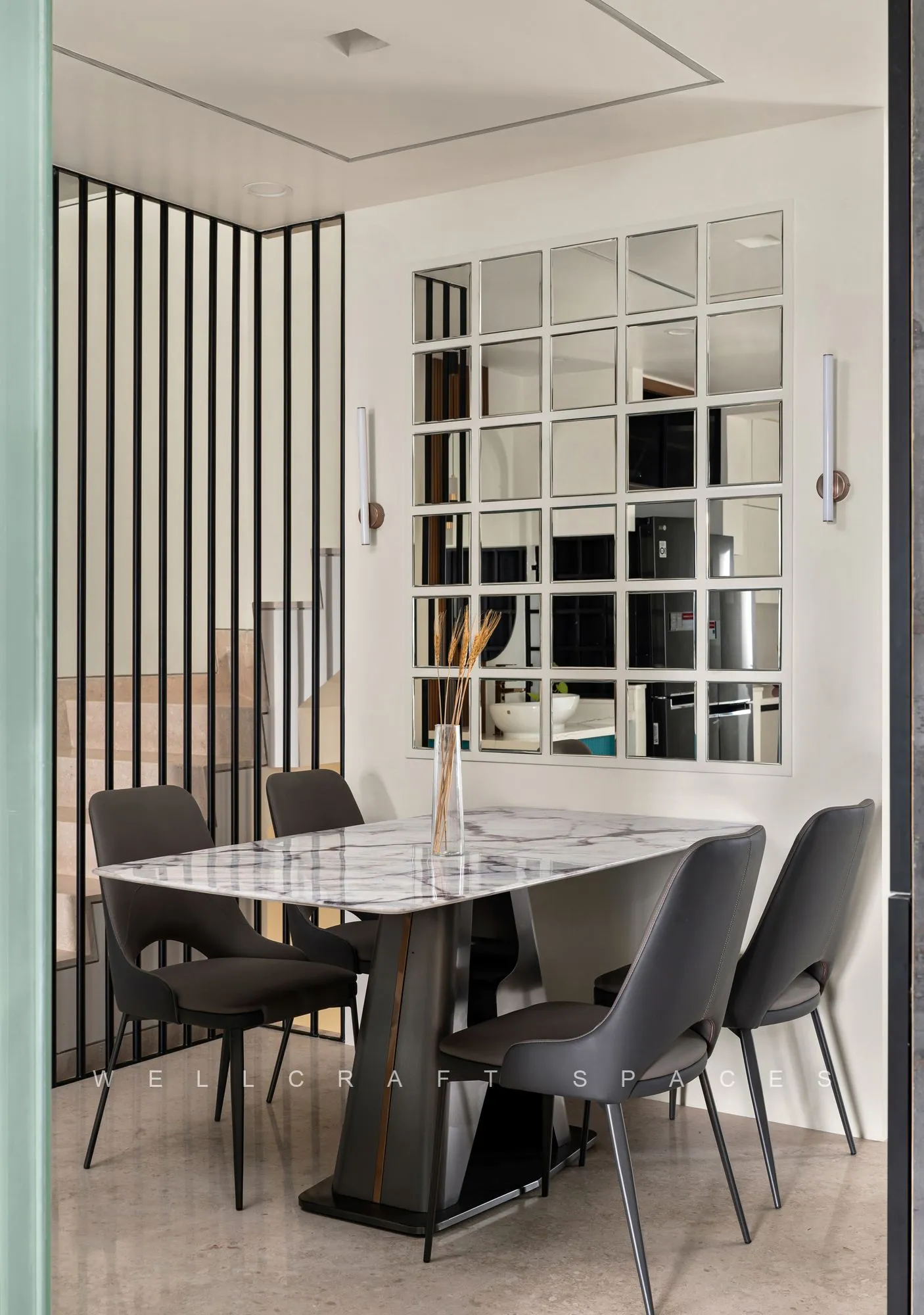 Dining table in veined marble with slate-grey upholstered chairs, framed by a slim black metal screen and a gridded mirror panel behind.