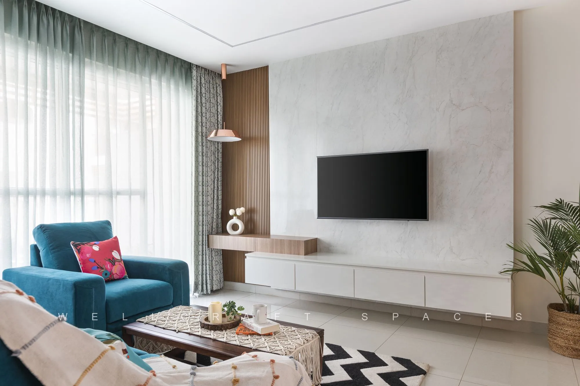 Wall-mounted television on a white panelled unit with a floating wooden ledge, seen past the teal sofa and a low coffee table.