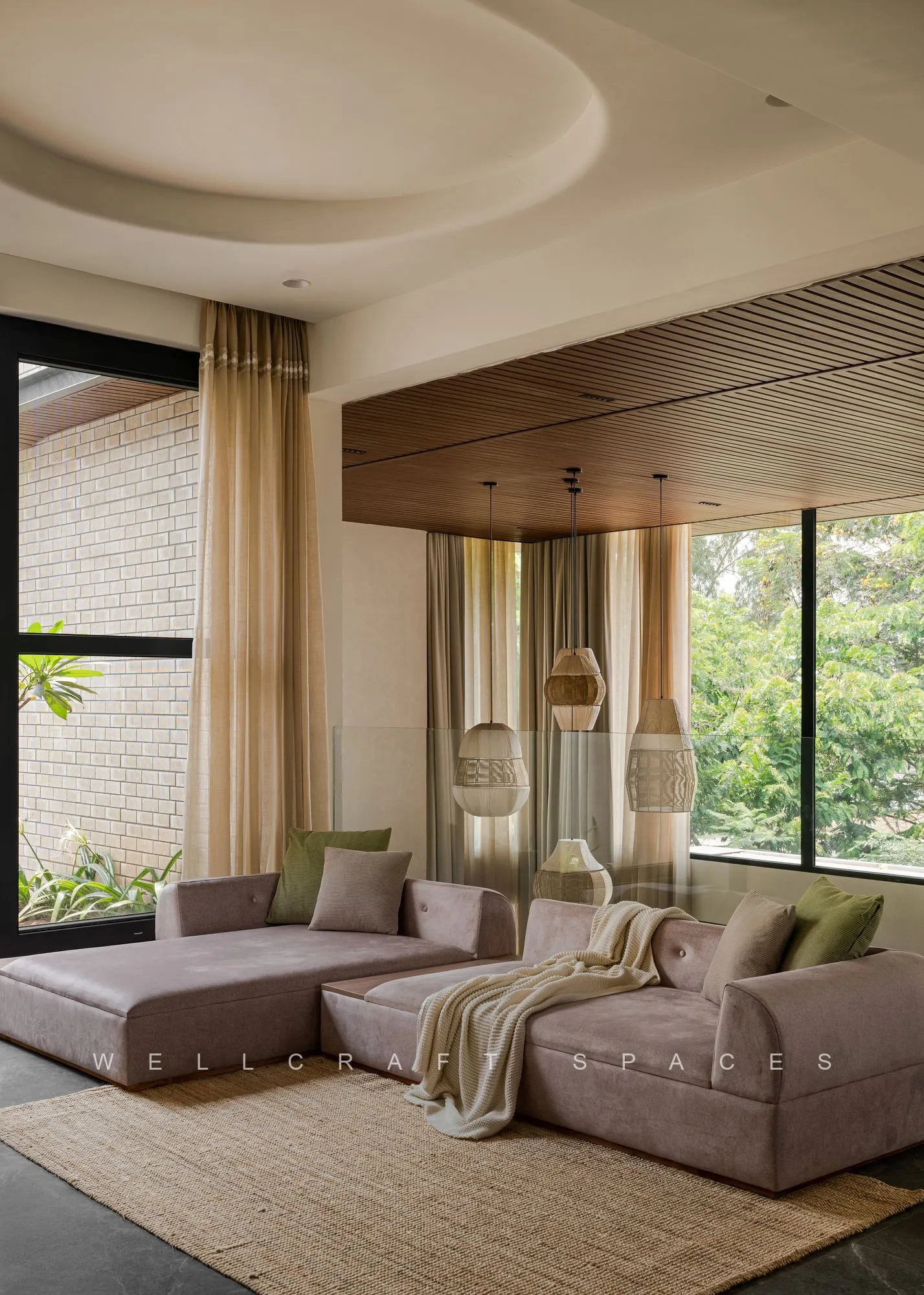 Deep grey modular sofa facing a wall of black-framed windows, with a knitted throw and a woven jute rug on charcoal stone flooring.