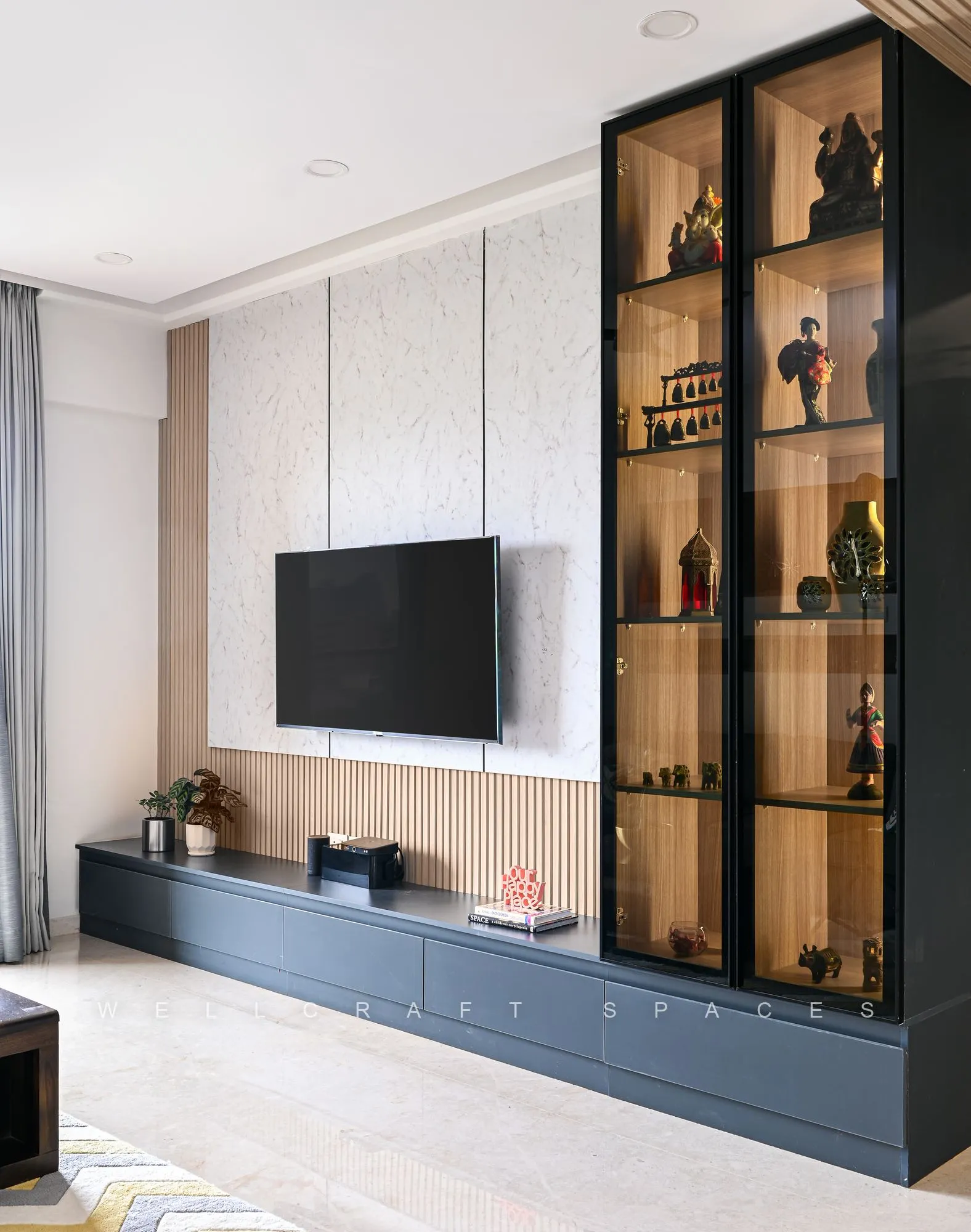 Navy media console with a wall-mounted television and a tall black-framed glass display cabinet on a fluted white panel.