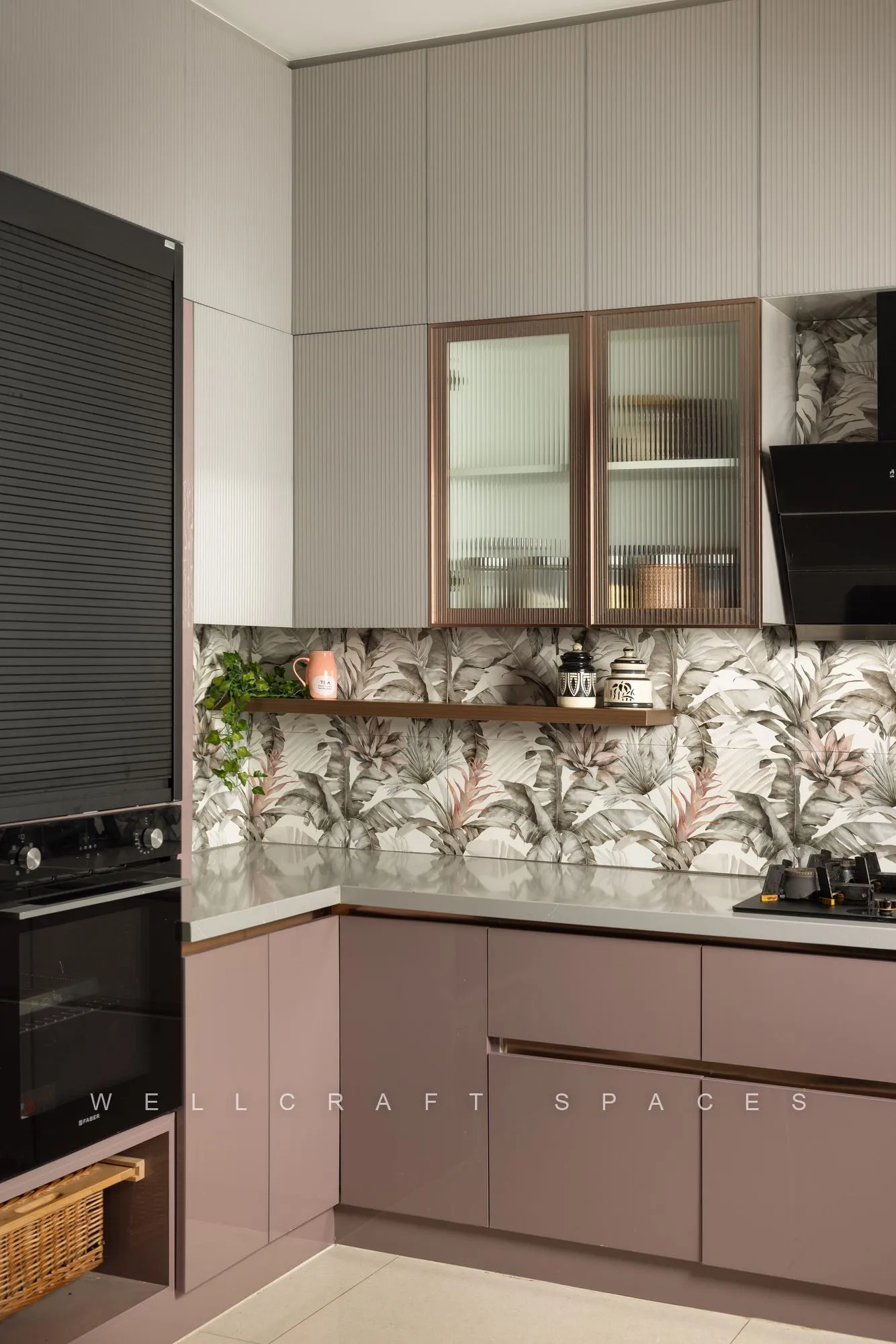L-shaped kitchen with mauve lower cabinetry, cream uppers, a built-in oven column and a leafy printed tile splashback.