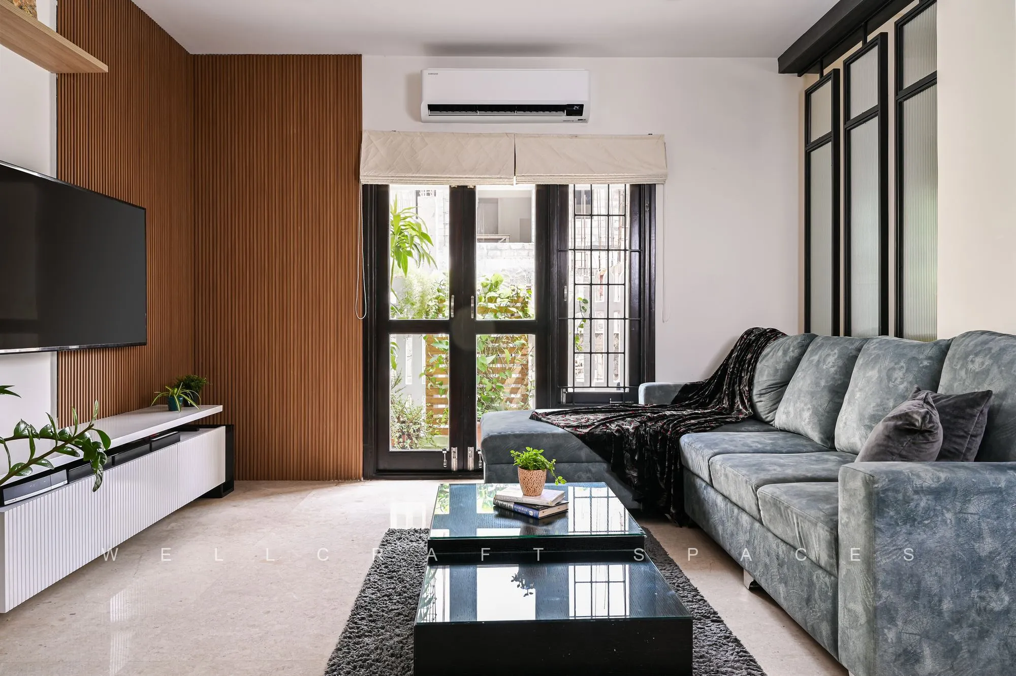 Family lounge with grey tufted sofas, a black marble coffee table and a slim wall-mounted television above a white ledge unit, backed by walnut panelling.