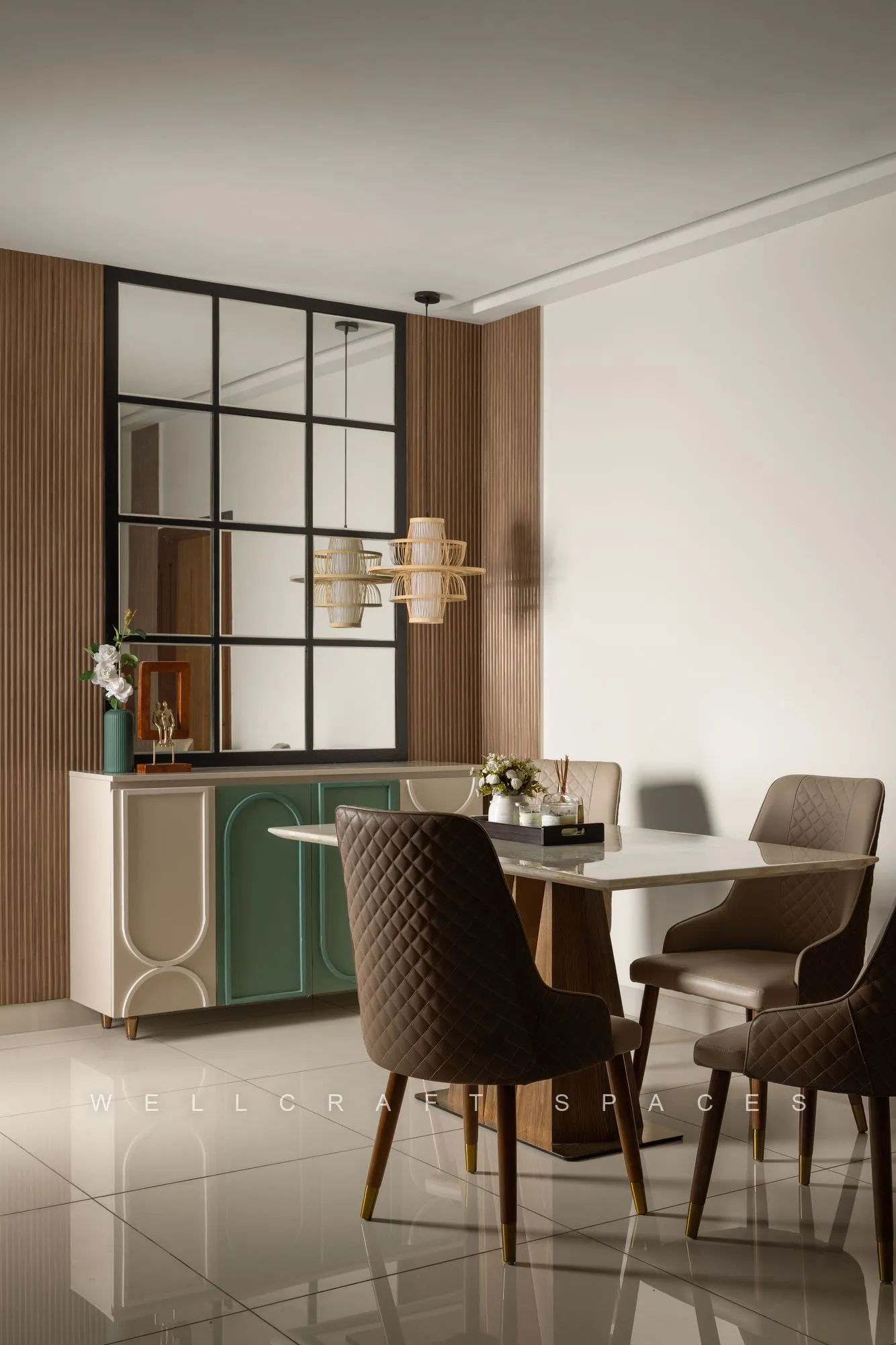 Dining table with dark leather chairs under a brass linear chandelier, beside a sage sideboard and a black grid glass partition.
