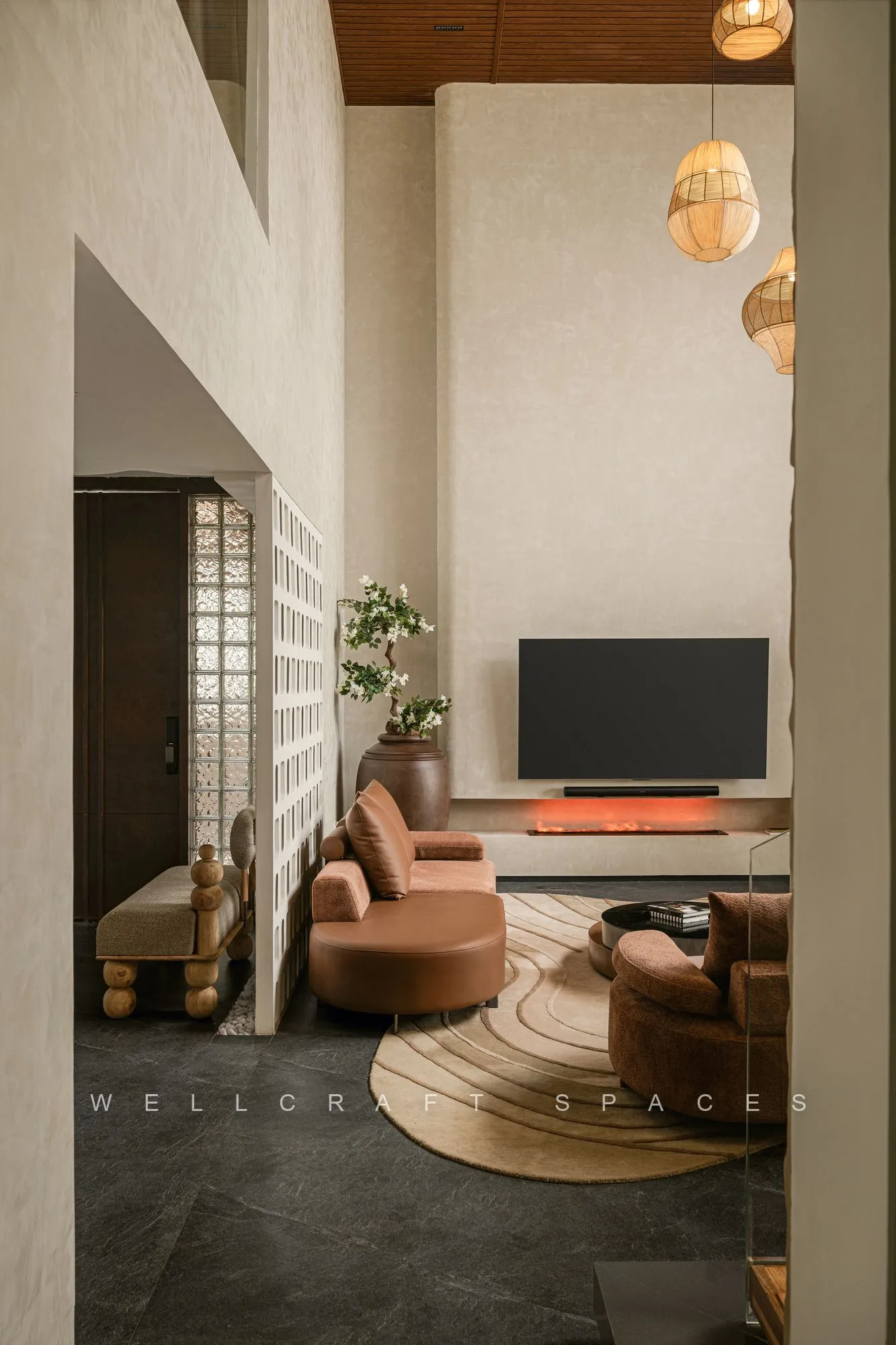 Family lounge with a curved rust sofa, round woven rug, wall-mounted television and rattan pendant lights under a double-height void.