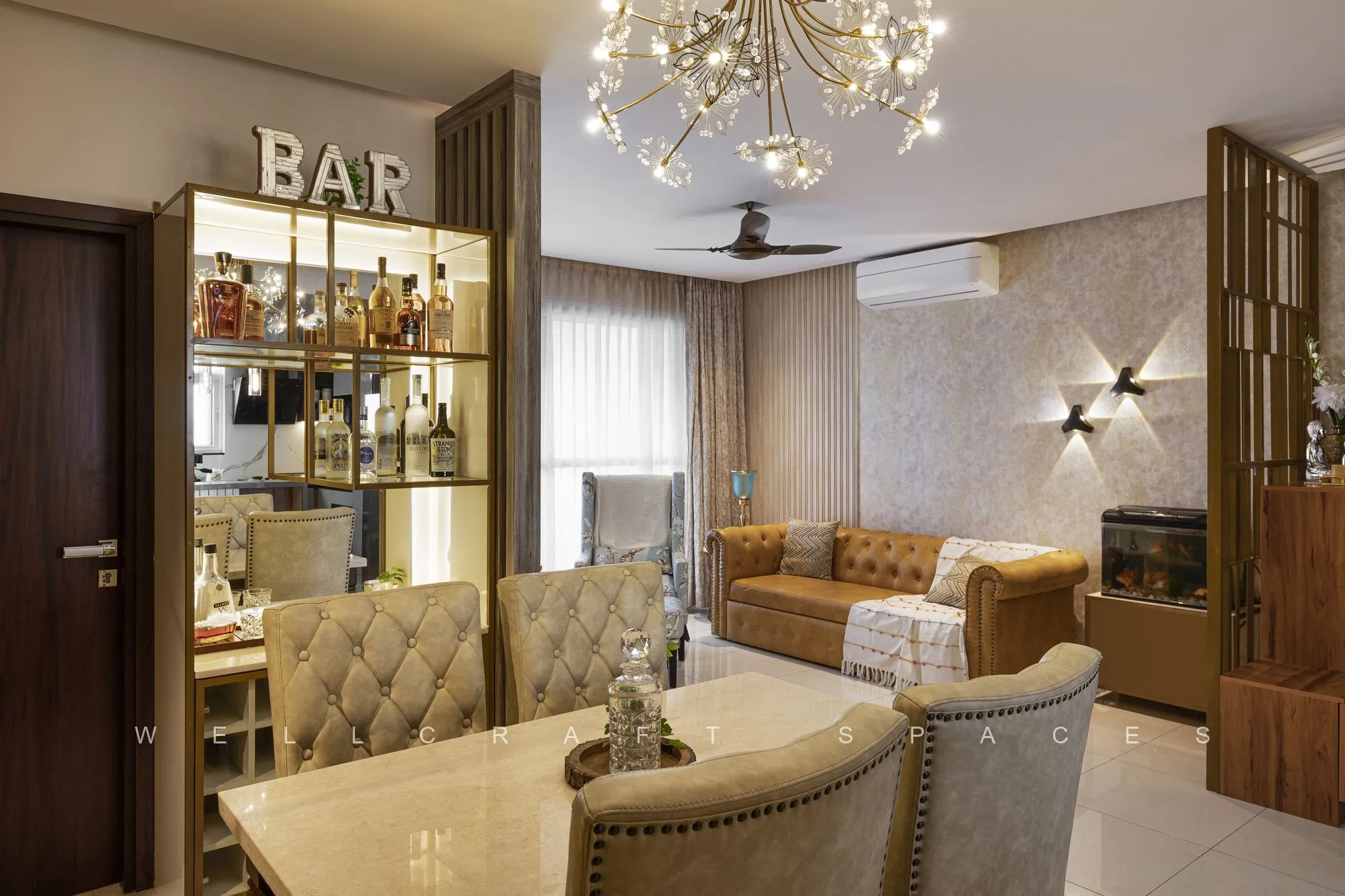 Living and dining seen together, with the tan leather sofa, tufted dining chairs and a crystal chandelier over the bar unit.