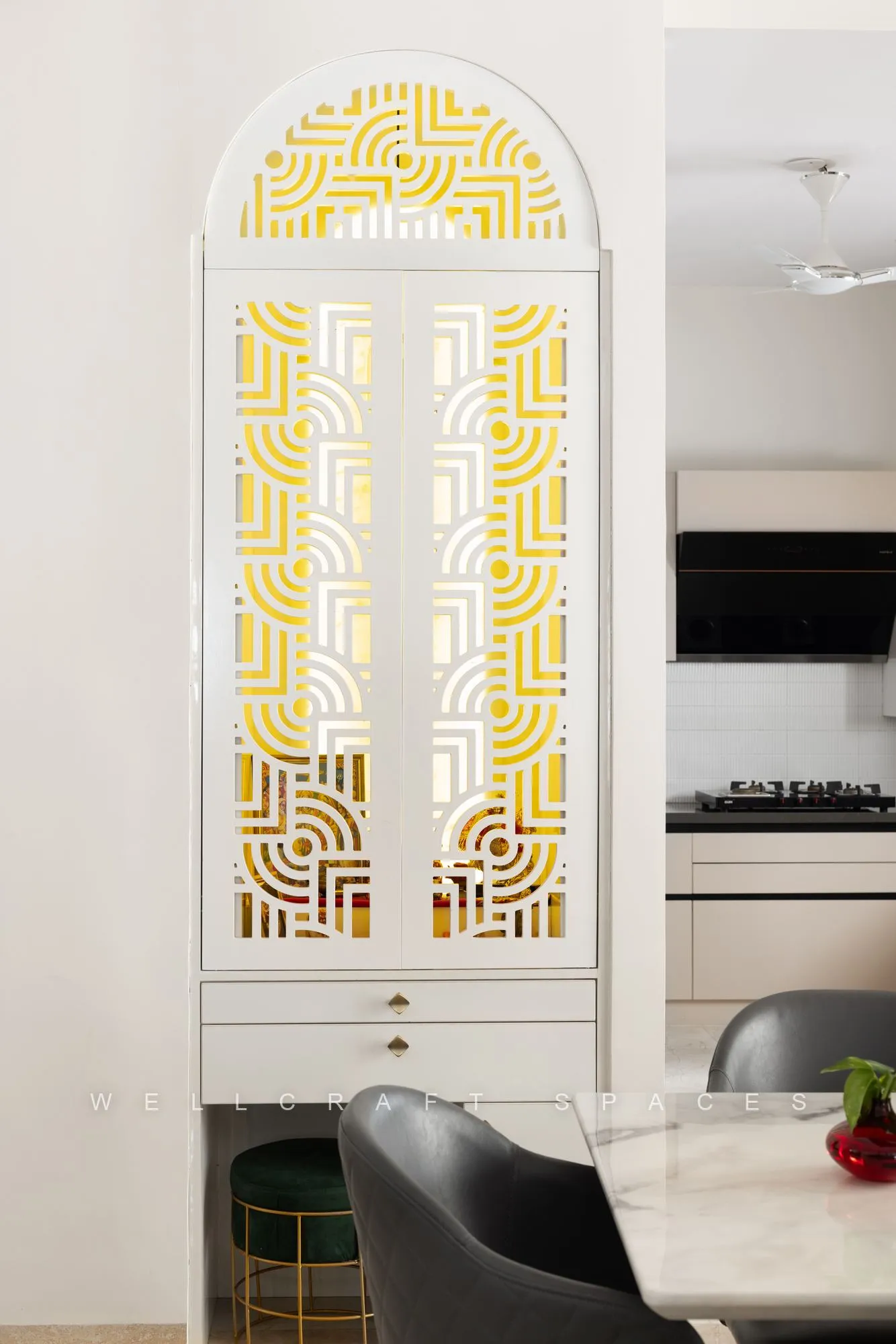Arched prayer alcove closed by carved shutters in white and mustard fretwork, set into cabinetry beside the kitchen counter.