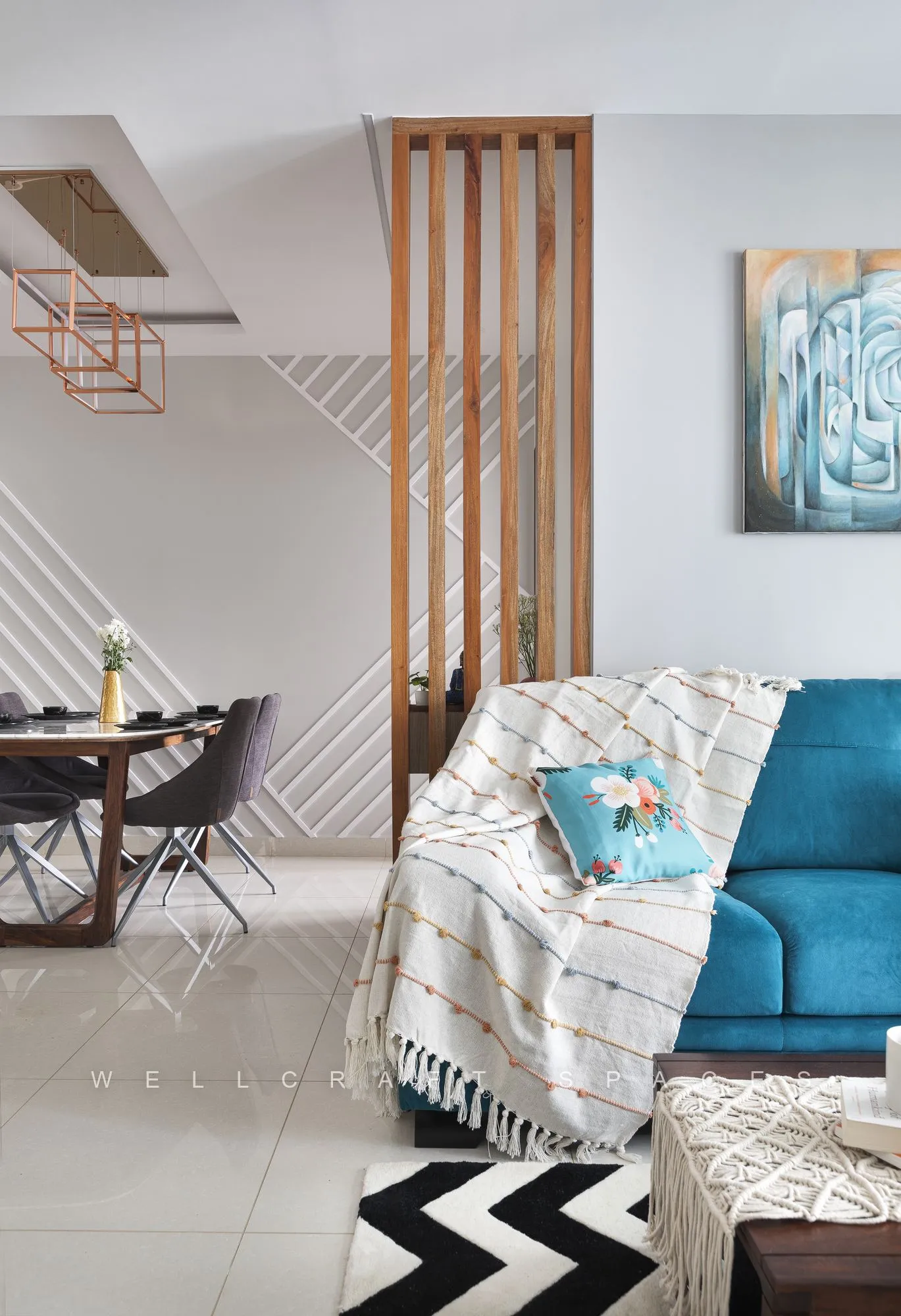 Dining table with black chairs behind a wood-and-metal slat screen, with the teal sofa and abstract canvas in the background.