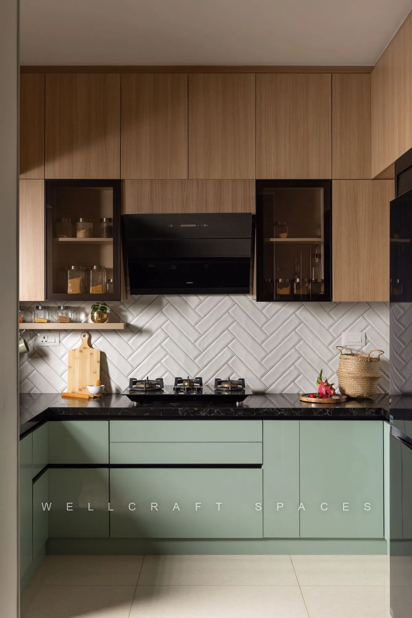 Sage-green base cabinets with black granite counters, teak overheads and a white herringbone tile backsplash around the hob.