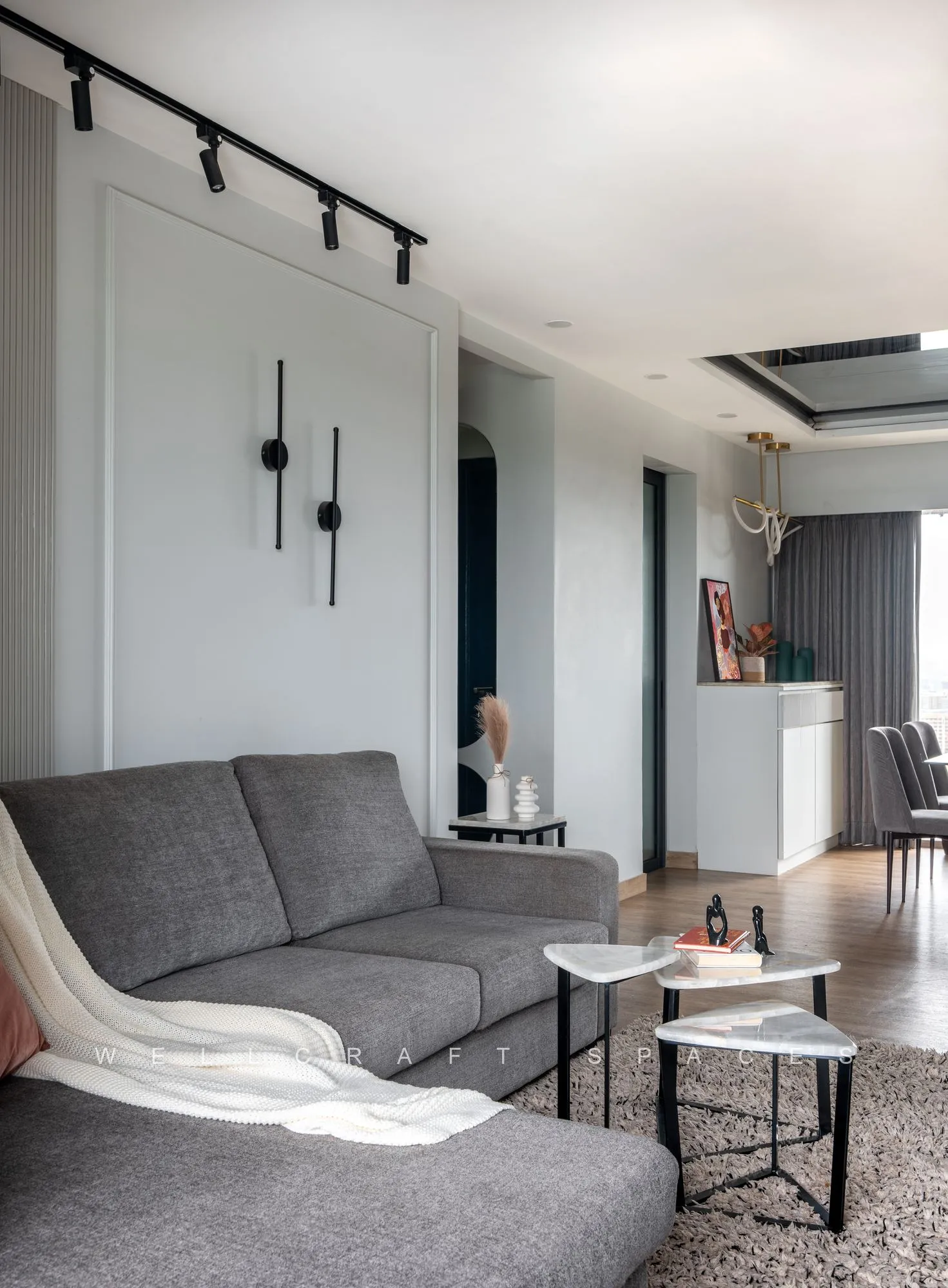 View across the lounge past the grey sofa and marble side tables toward the dining area and its white sideboard.
