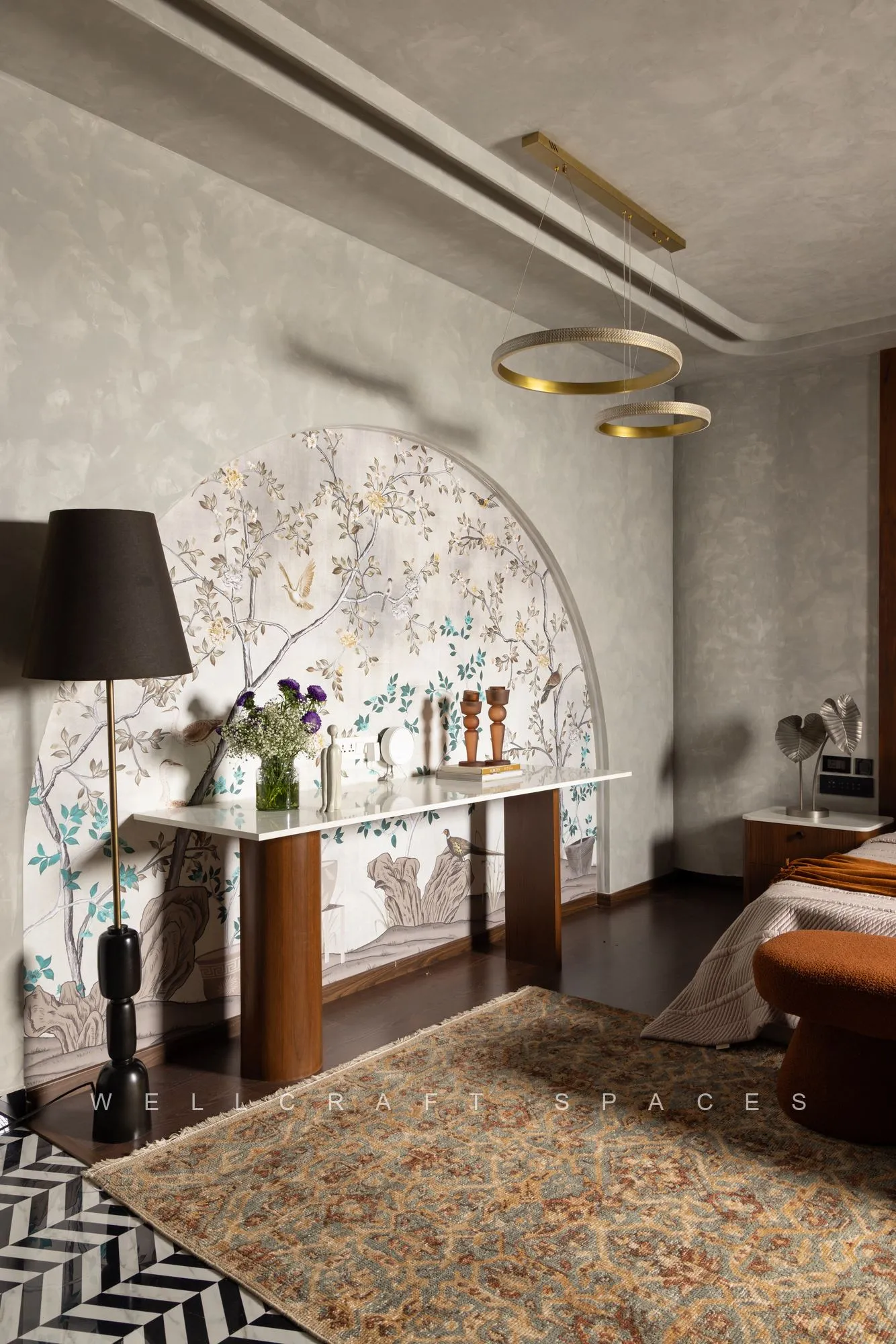 Master bedroom dressing side with an arched mirror, slim console, black shaded lamp and a patterned rug over dark flooring.