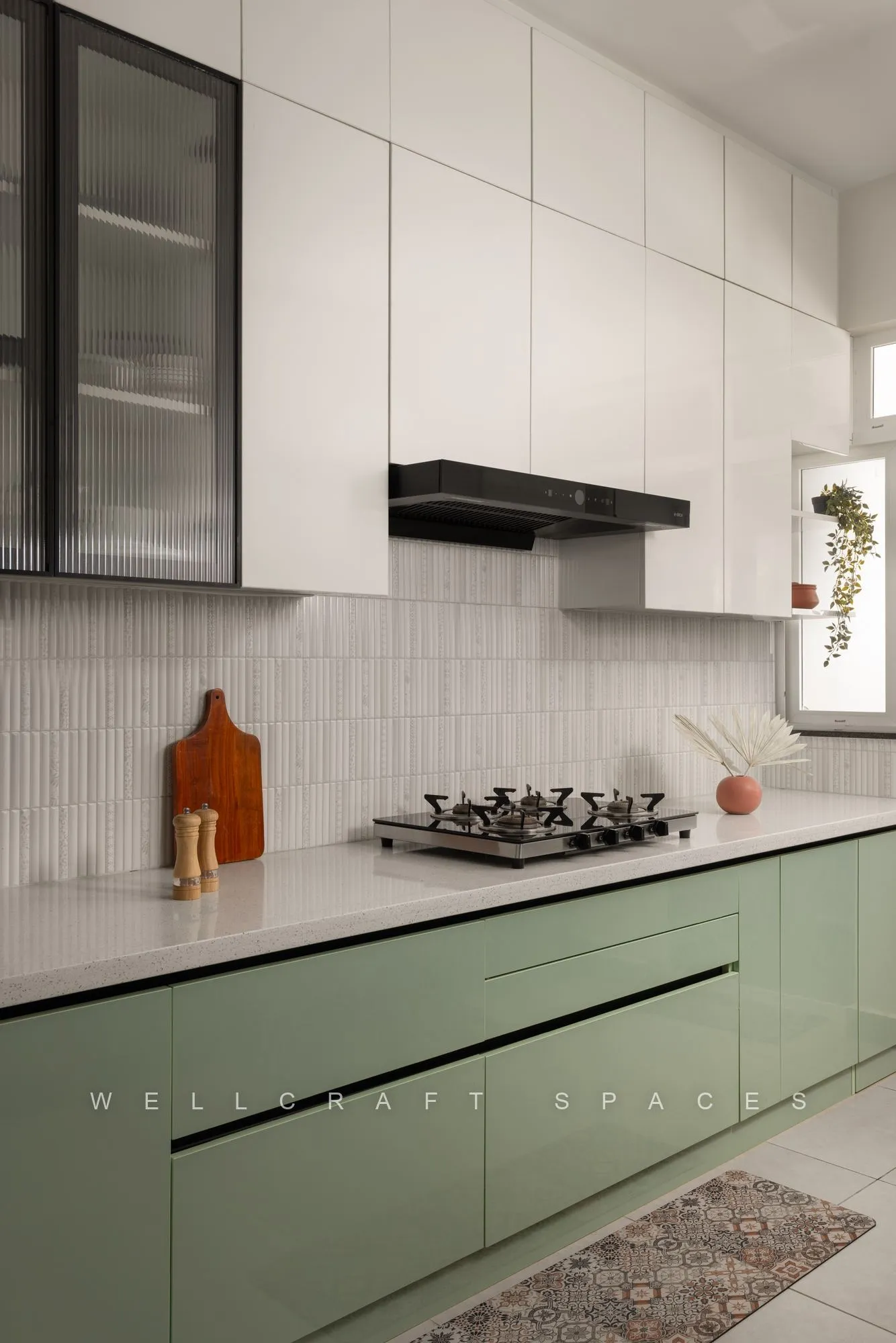 Sage-green handleless kitchen with white overhead cabinets, a stacked tile backsplash, black chimney and a runner on the floor.