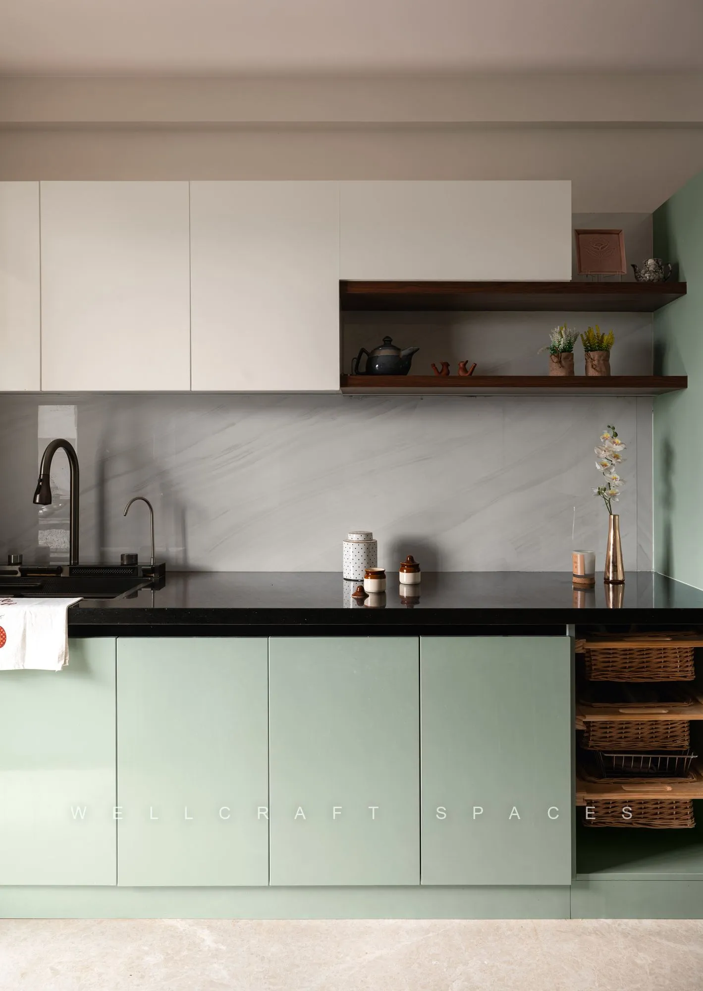 Kitchen run in sage green glossy shutters with black granite counters, a marble-effect backsplash and open walnut shelves holding copperware.