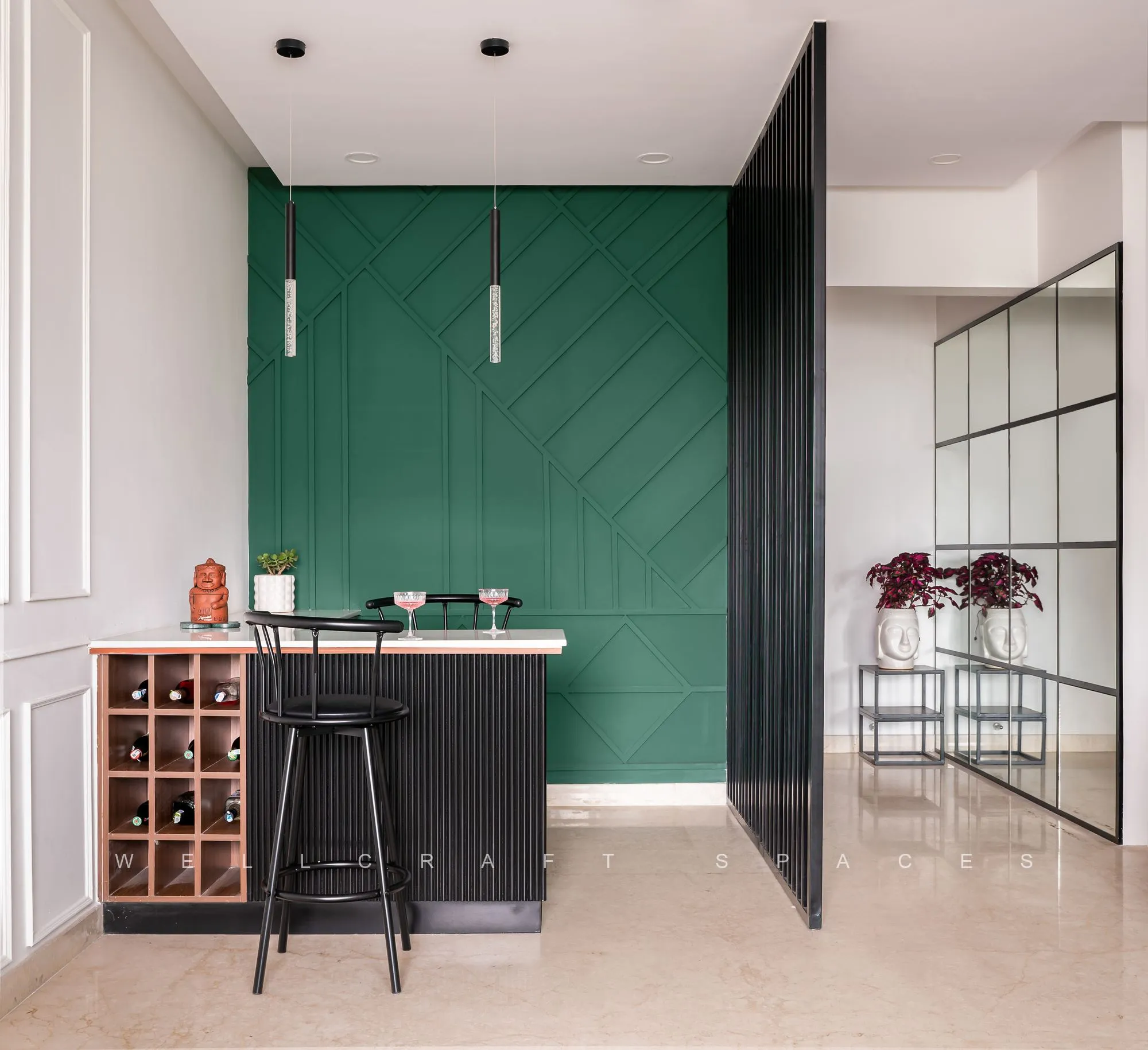 Bar counter in deep green chevron panelling with a stone top, black metal bar stools and an open wine rack built into the adjoining cabinetry.