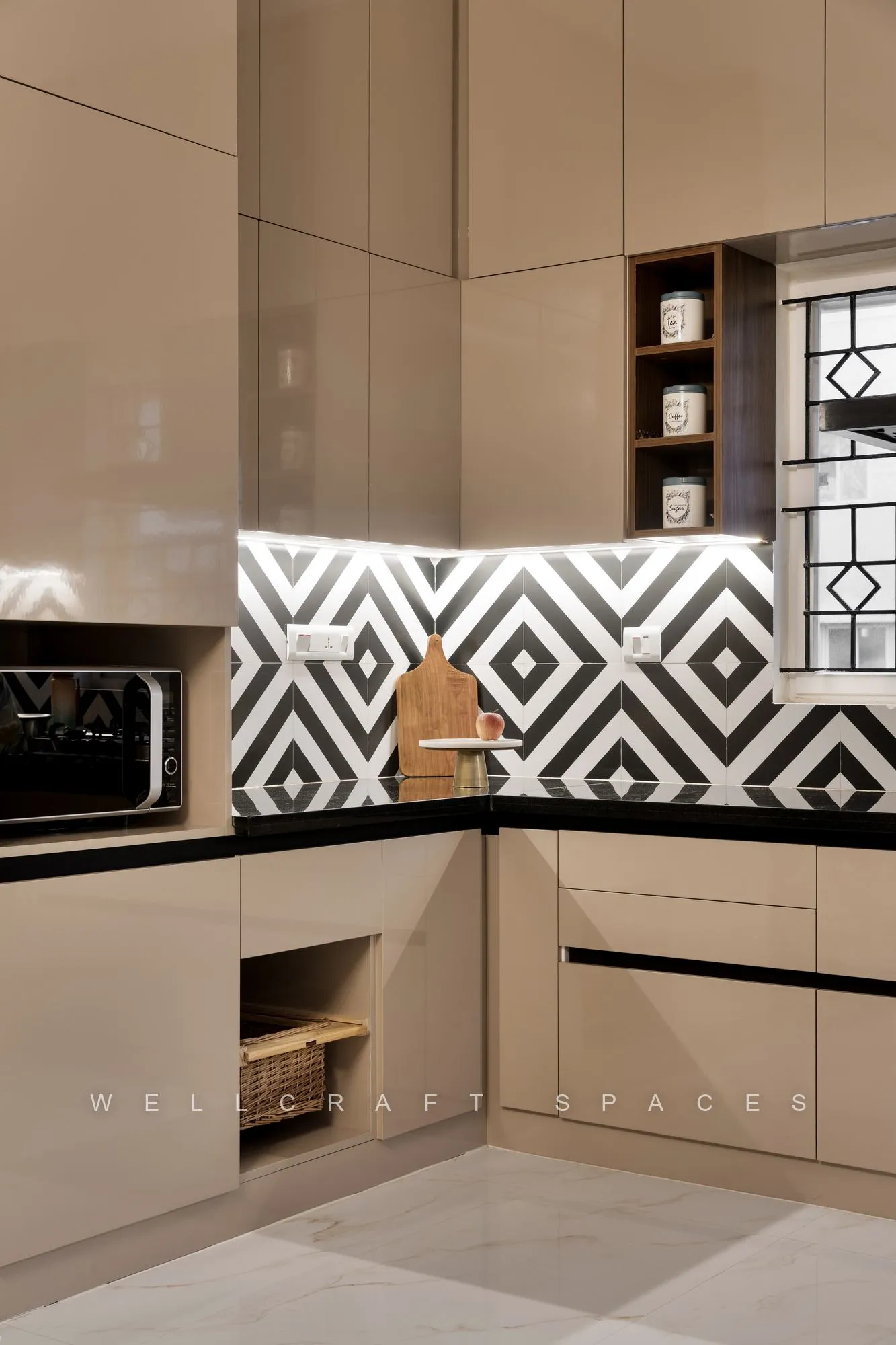 Compact kitchen in glossy beige shutters with black counters, a bold black-and-white geometric tile backsplash and a built-in microwave niche.