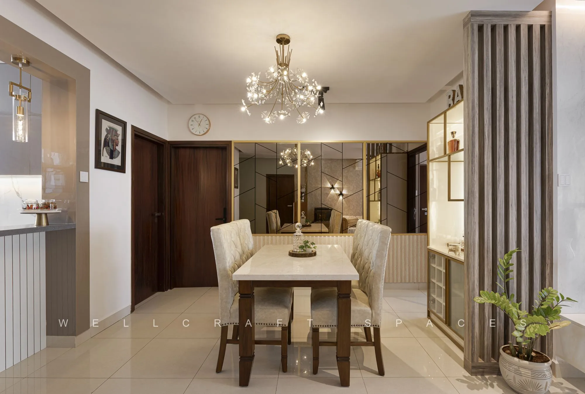 Dining table with cream upholstered chairs under a crystal chandelier, framed by a wooden door and a mirrored feature wall.